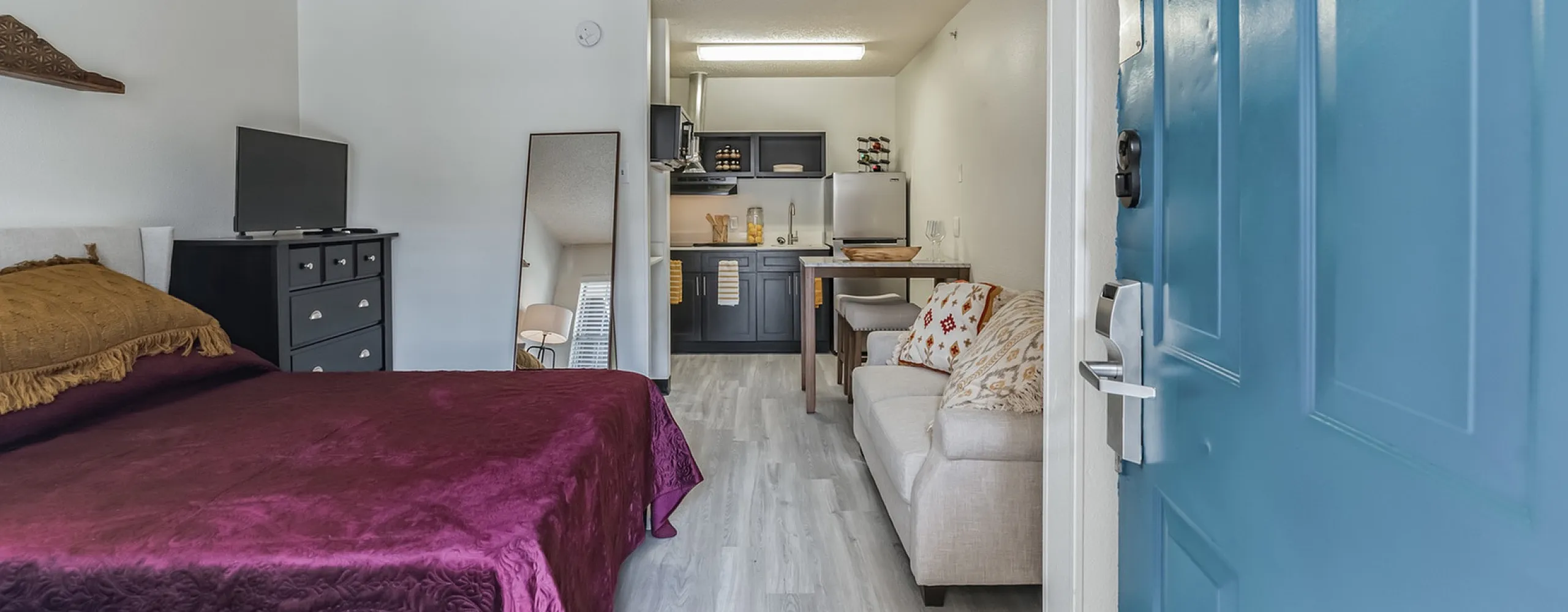 Wide-angle view of a modern Vivo Living Willowbrook studio apartment featuring an open-concept layout with wood-style flooring, a sleek kitchen, and a bright living area designed for professional living.