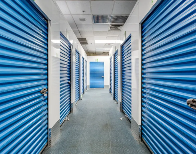 Modern self-storage facility with secure, vibrant blue roll-up doors lining a clean, well-lit hallway.
