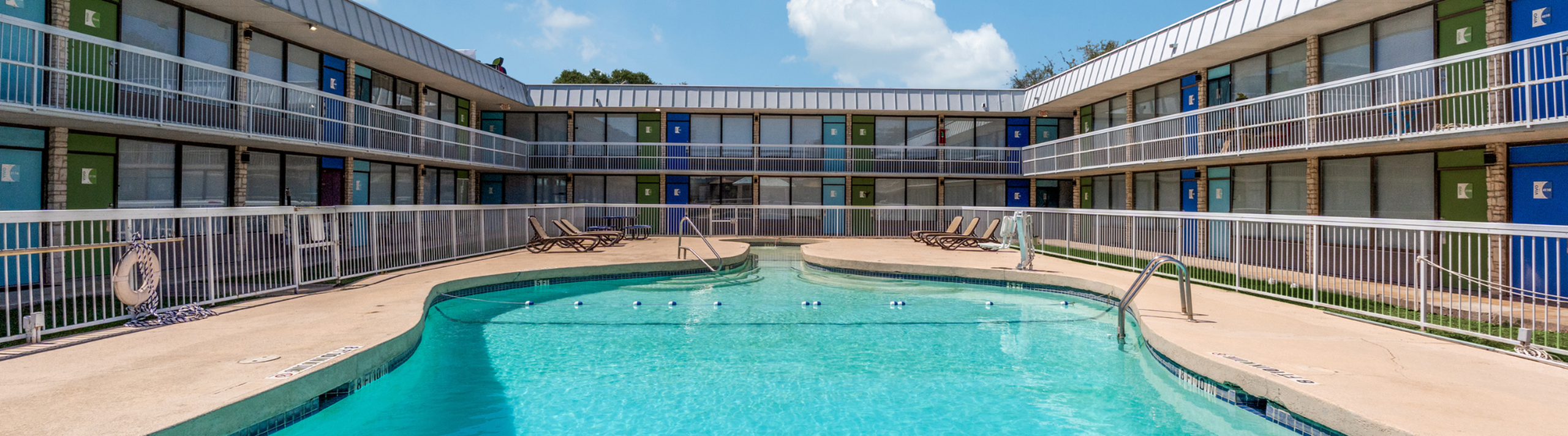 Inviting apartment complex featuring a sparkling outdoor pool, sun-drenched lounge chairs, and vibrant exterior colors.