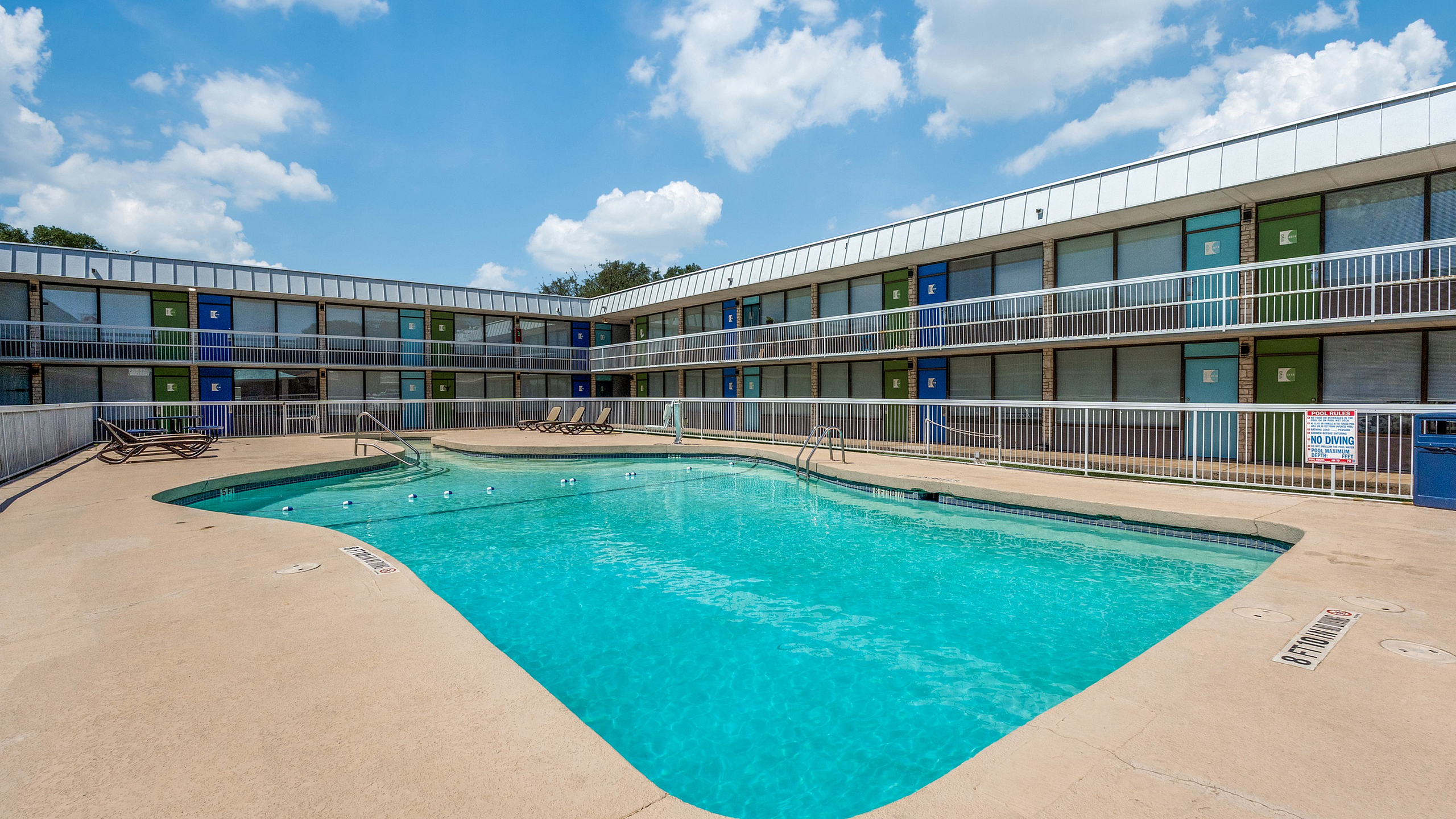 Inviting swimming pool area in a modern apartment complex, featuring vibrant doors and relaxing lounge chairs under a clear blue sky.