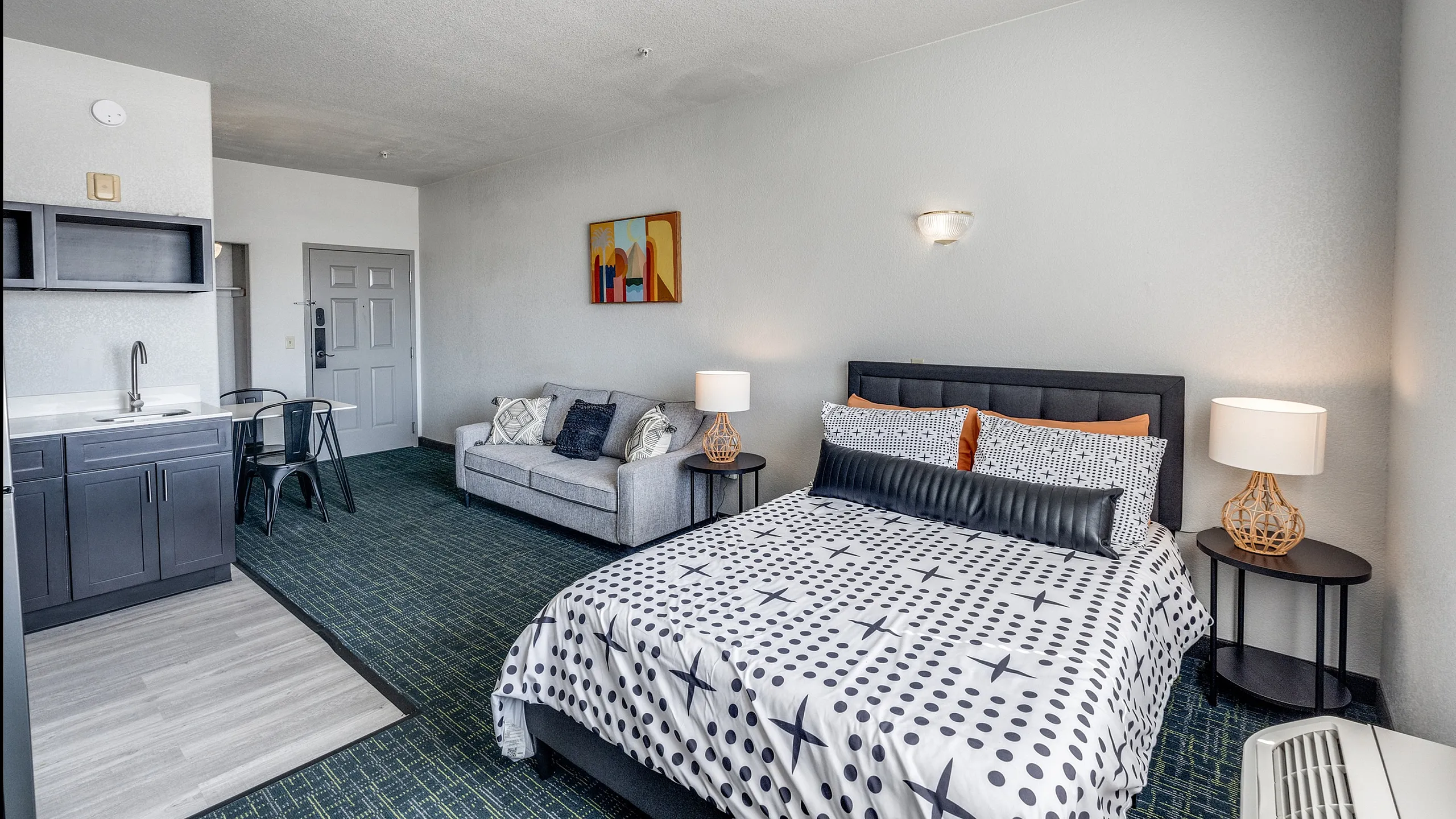 Chic studio apartment with modern decor, featuring a plush bed, cozy seating area, and compact kitchenette.