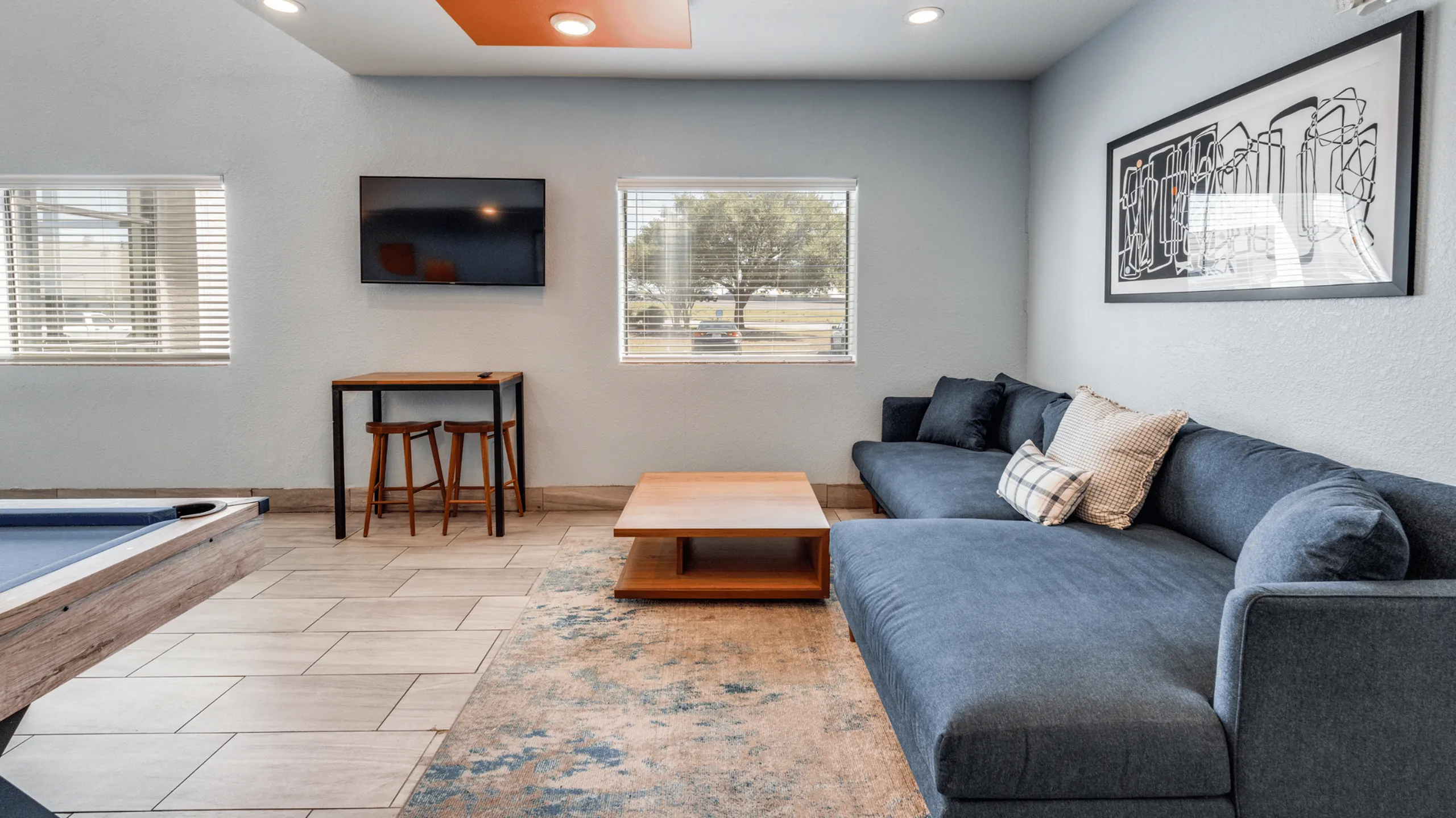 Inviting living room with chic blue sofa, modern artwork, and large windows offering natural light. Stylish entertainment area with wall-mounted TV and cozy seating.
