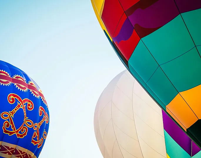 Vibrant close-up of colorful hot air balloons against a clear blue sky, showcasing intricate patterns and bold hues.