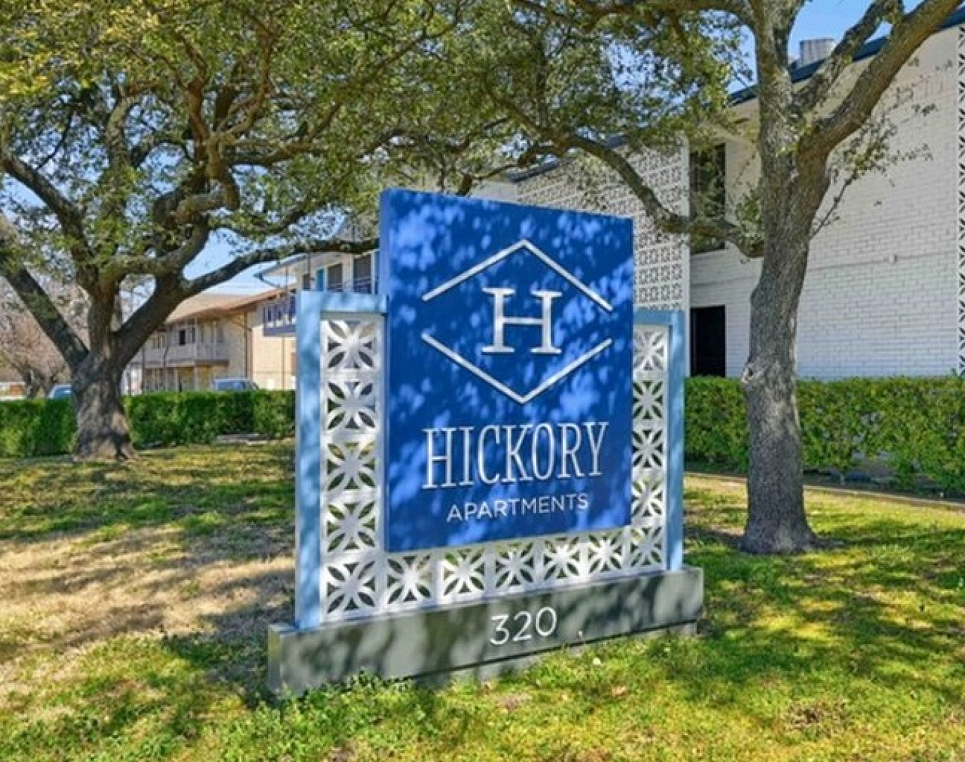 Inviting entrance to Hickory Apartments featuring a modern sign surrounded by lush greenery and tall trees.