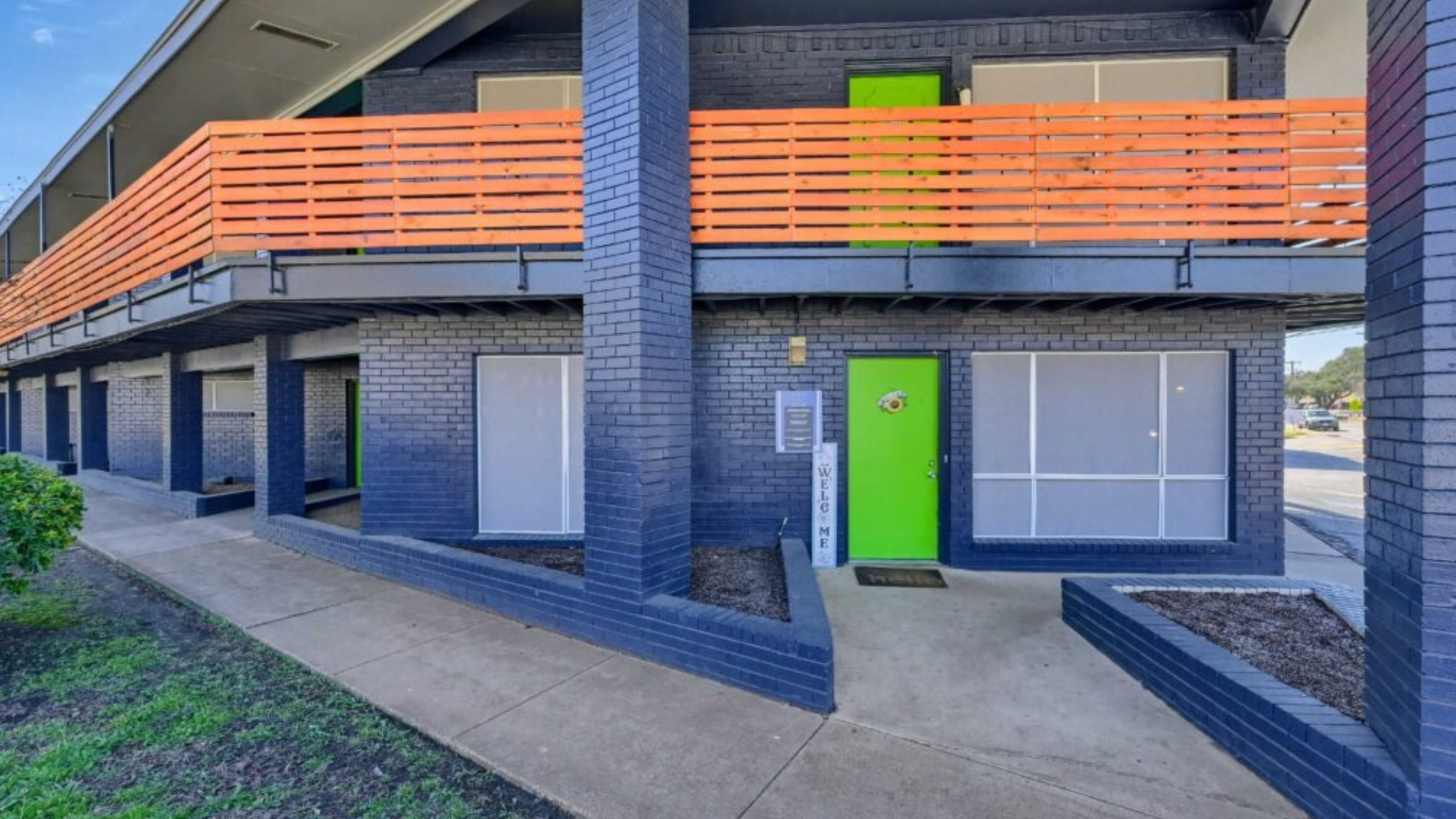 Modern apartment entrance featuring vibrant green doors, sleek gray brick facade, and bold orange railing.