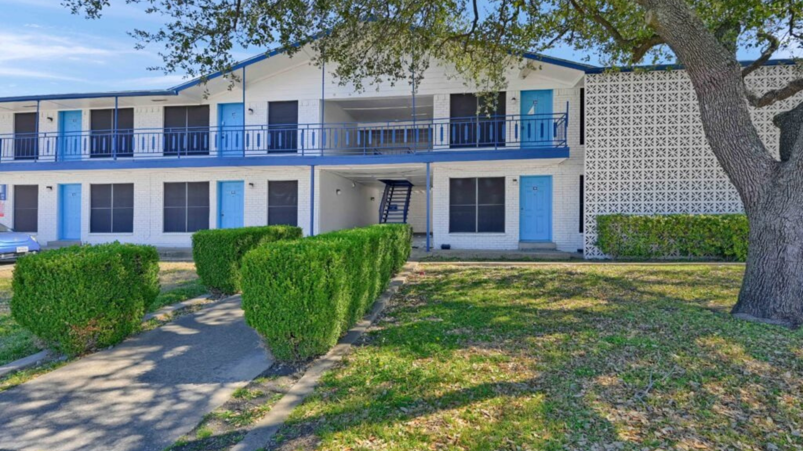 Charming two-story apartment building with vibrant blue doors and lush greenery in a serene neighborhood.
