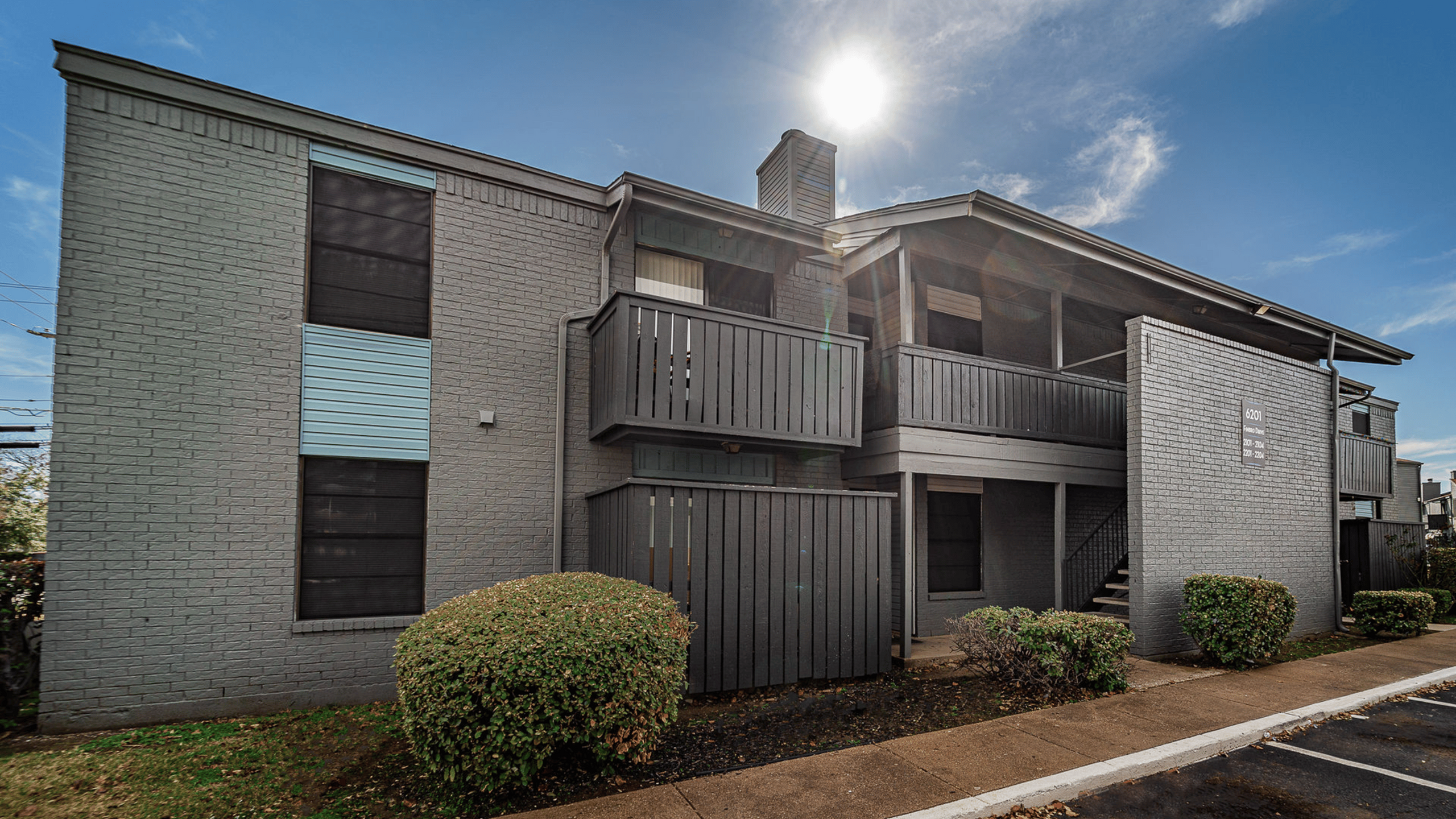 Modern apartment building with stylish gray brick facade, private balconies, and inviting outdoor design under a bright blue sky.