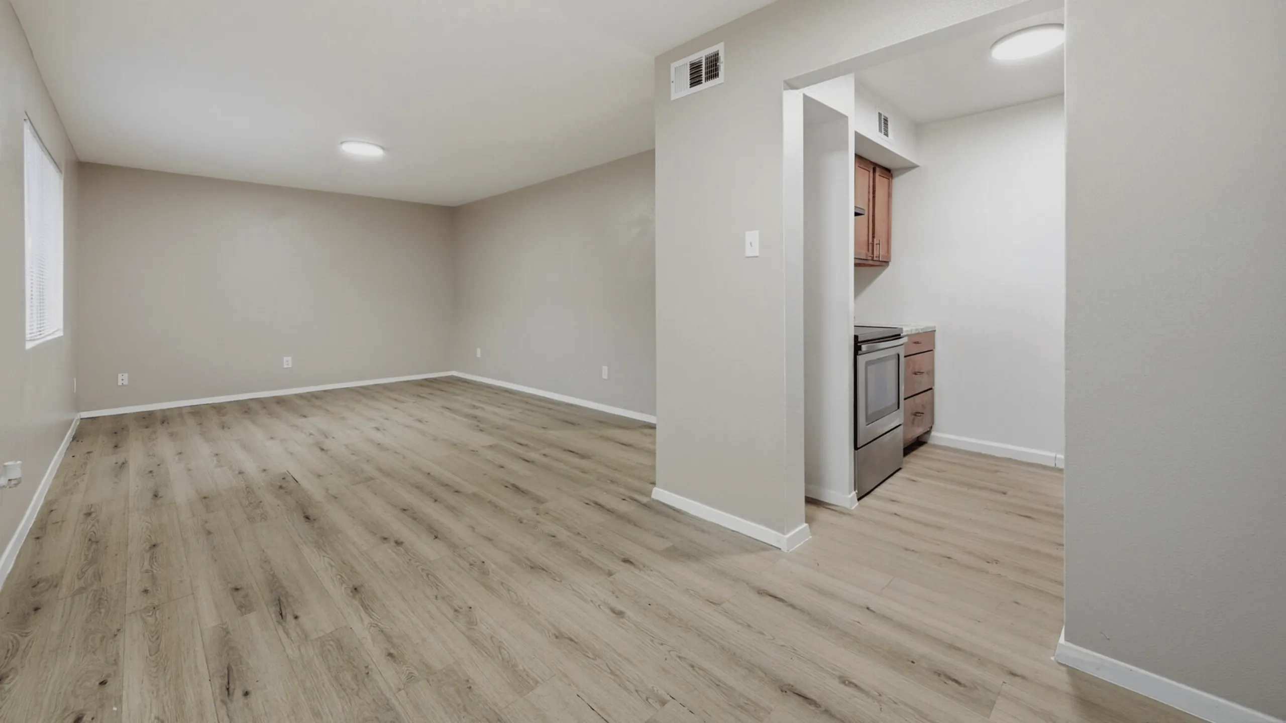 Elegant apartment interior showcasing a spacious open-plan living area with modern wooden flooring and a sleek kitchen entrance.