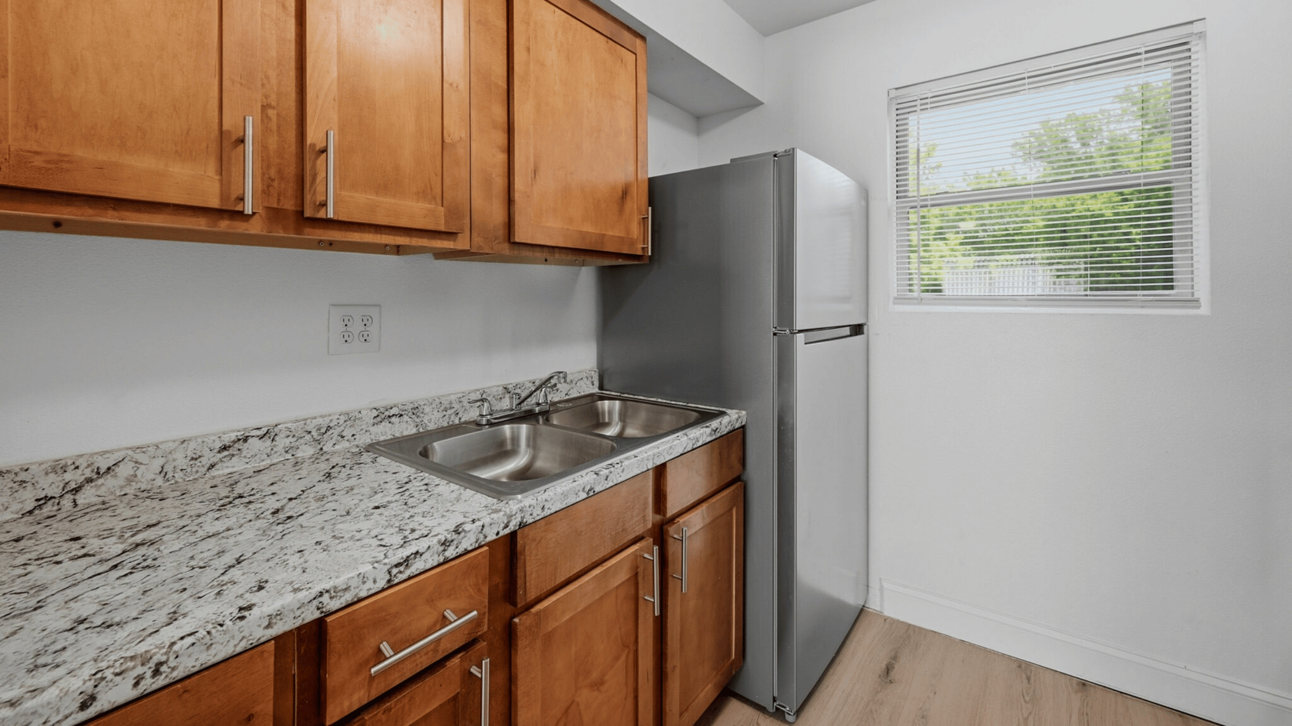 Bright and modern kitchen with sleek stainless steel fridge, elegant granite countertops, and warm wooden cabinetry.