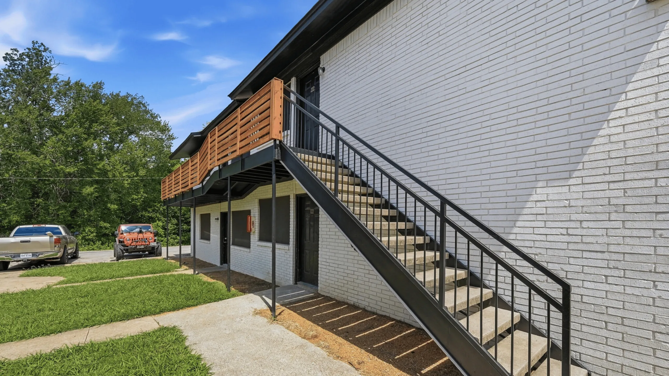 Charming apartment exterior featuring a modern staircase, sleek white brick facade, and vibrant green landscaping.