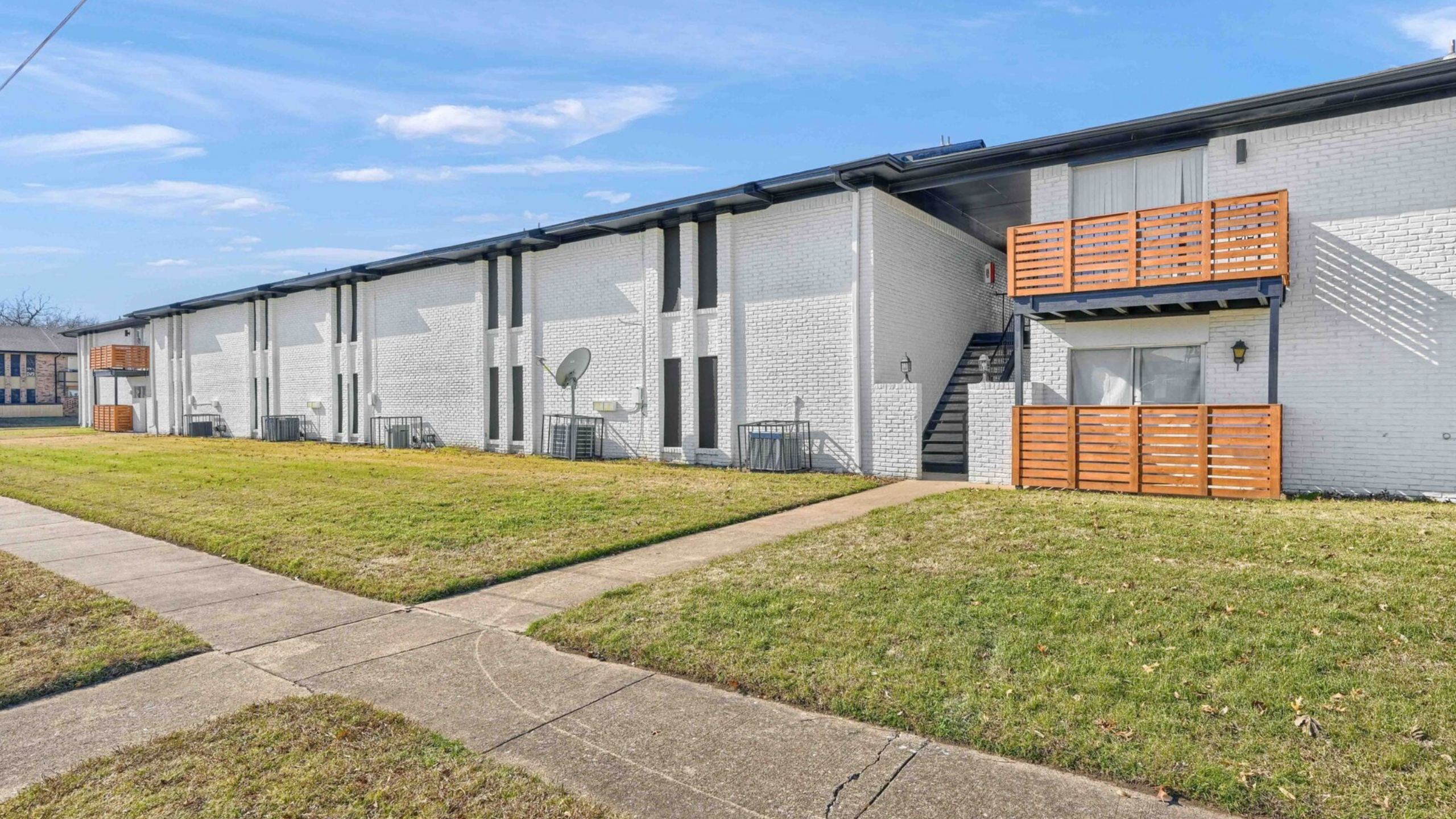 Charming white brick apartment building with modern wood accents, featuring spacious green lawns and inviting walkways.