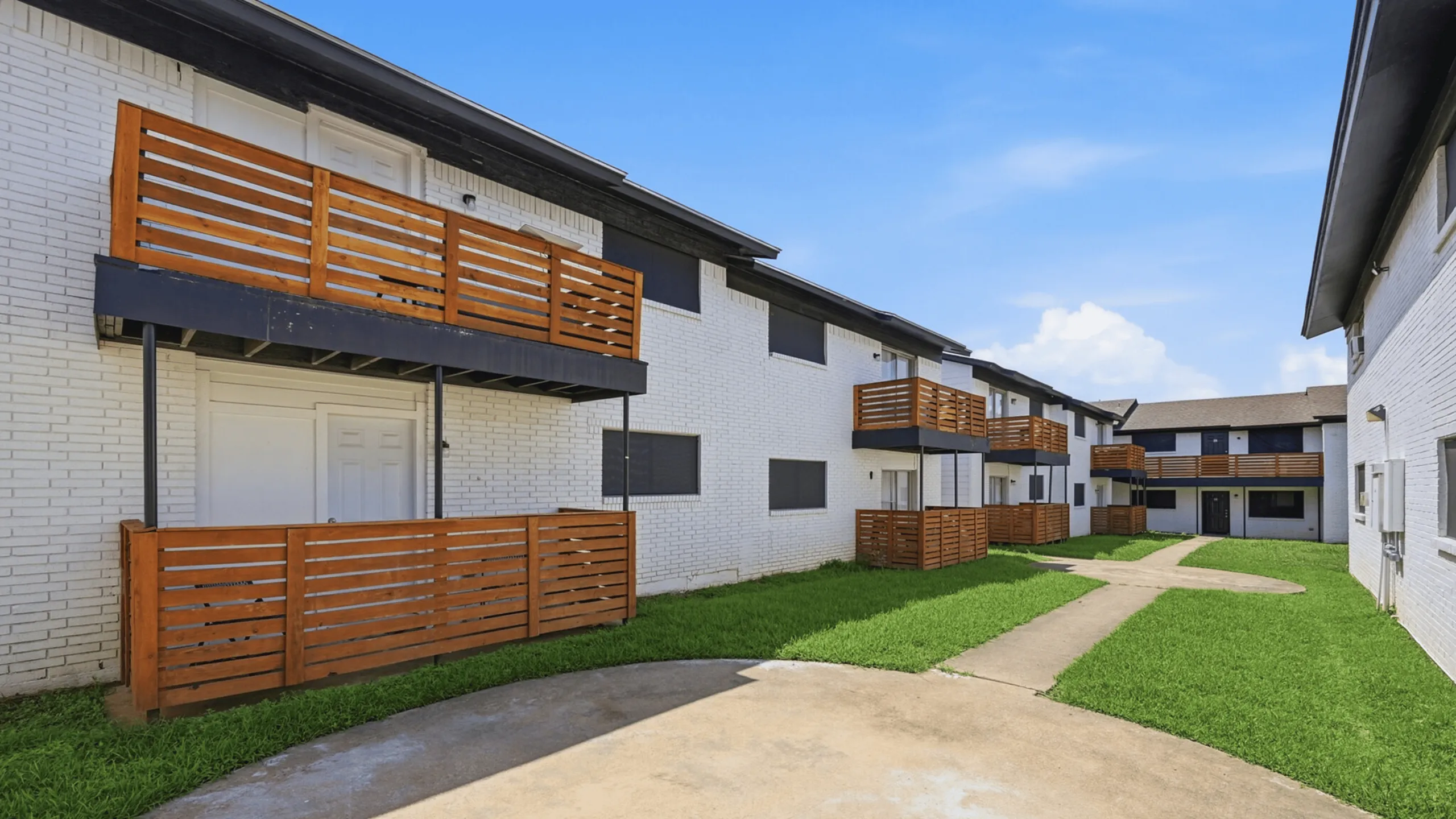 Charming apartment complex with modern wooden balconies and well-maintained green lawn under a clear blue sky.
