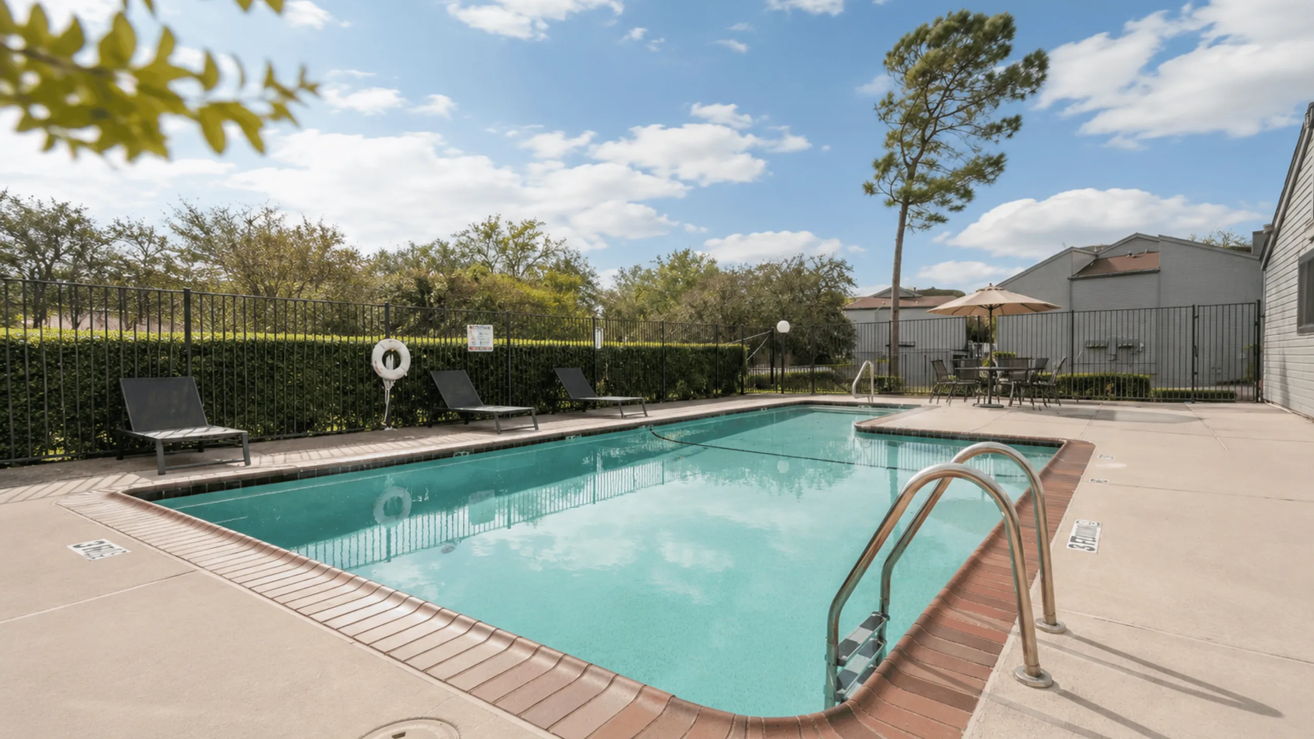 Inviting outdoor pool area with lounge chairs and umbrellas, surrounded by lush greenery and clear blue skies.