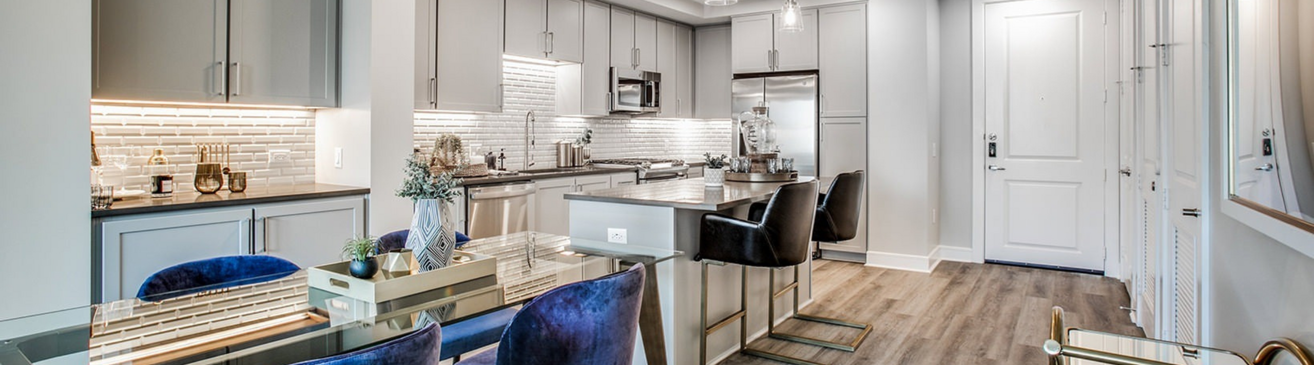 Luxurious modern kitchen with sleek grey cabinetry, stainless steel appliances, and elegant glass dining area offering a stylish urban living space.