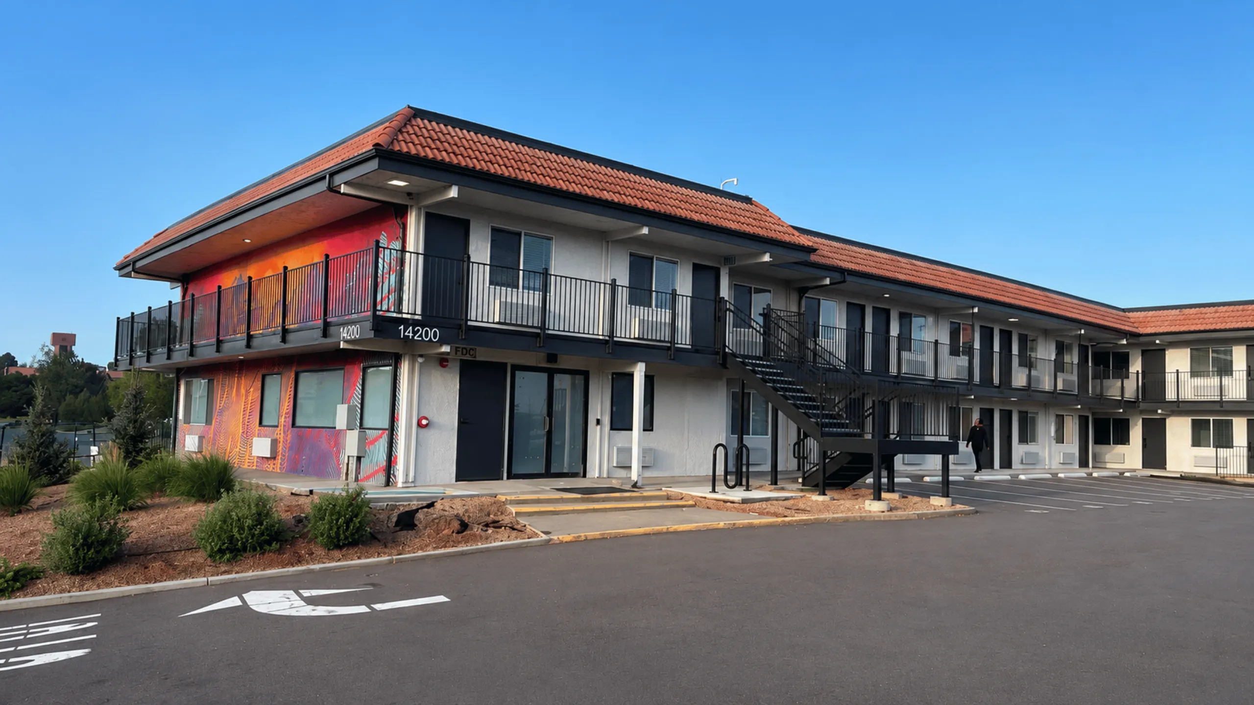 Modern two-story apartment building with vibrant exterior artwork, spacious balconies, and ample parking space.
