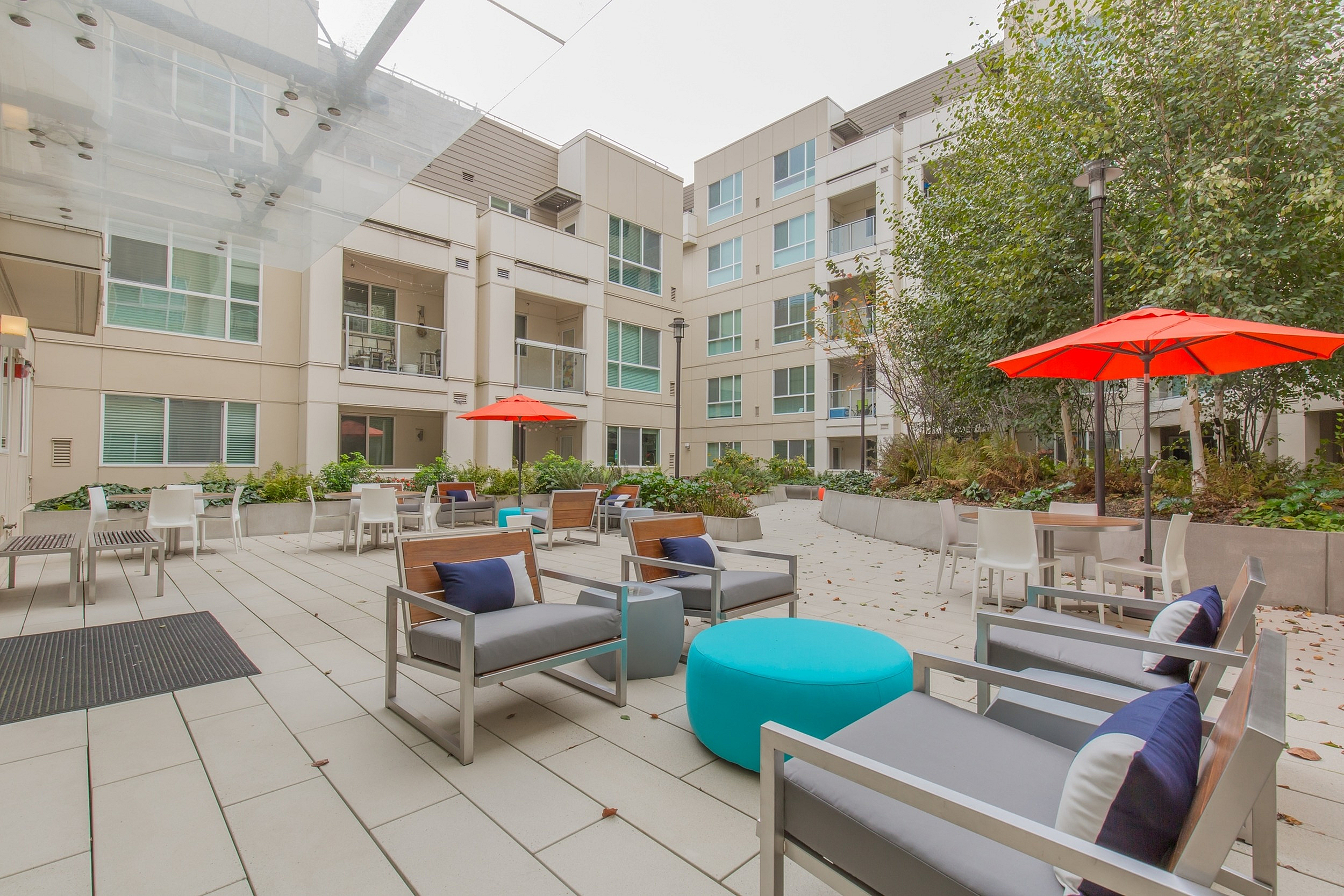 Modern apartment courtyard featuring stylish seating, vibrant red umbrellas, lush greenery, and inviting outdoor space for relaxation and socializing.