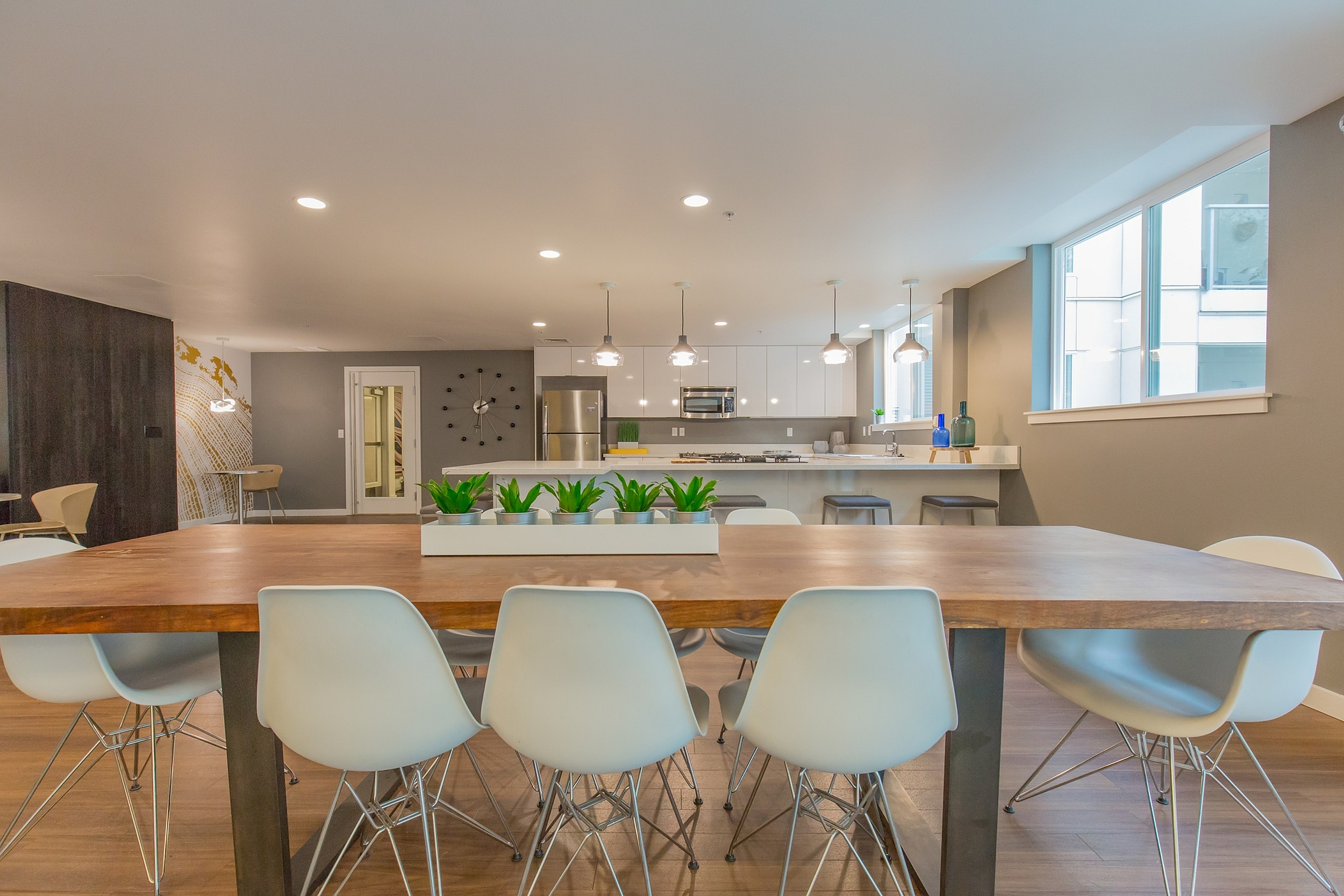 Modern open-concept kitchen and dining area with stylish white chairs, wooden table, pendant lighting, and sleek stainless steel appliances.