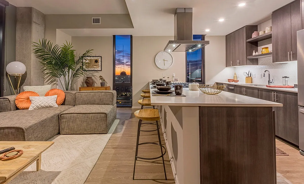 Elegant open-concept living room and kitchen with modern decor, featuring a sunset cityscape view through tall windows.