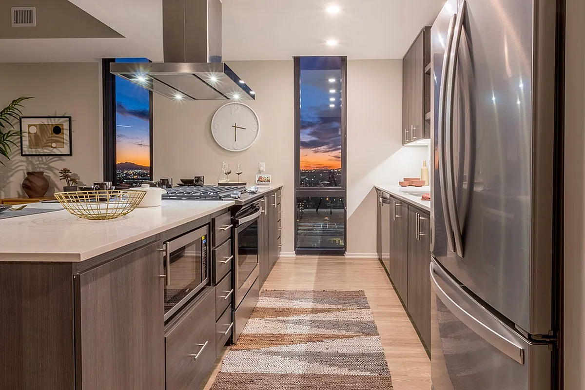 Contemporary kitchen with sleek stainless steel appliances, warm wood cabinetry, and a stunning sunset view through the window.