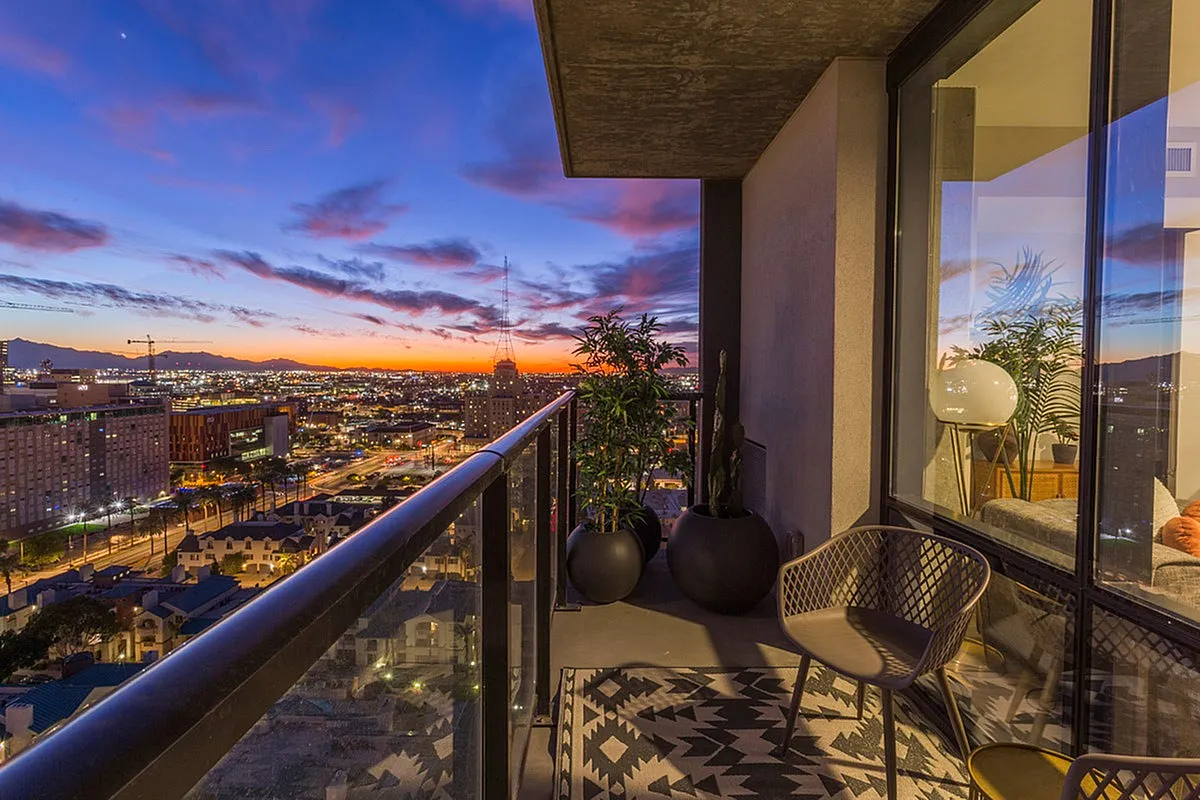 Luxurious apartment balcony offering stunning cityscape views at sunset, with modern outdoor seating and stylish decor.