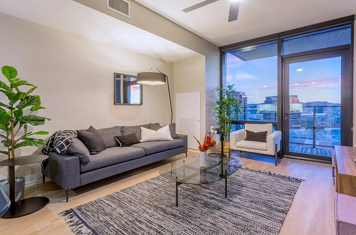 Modern living room with sleek gray couch, stylish decor, and panoramic city views through expansive windows.