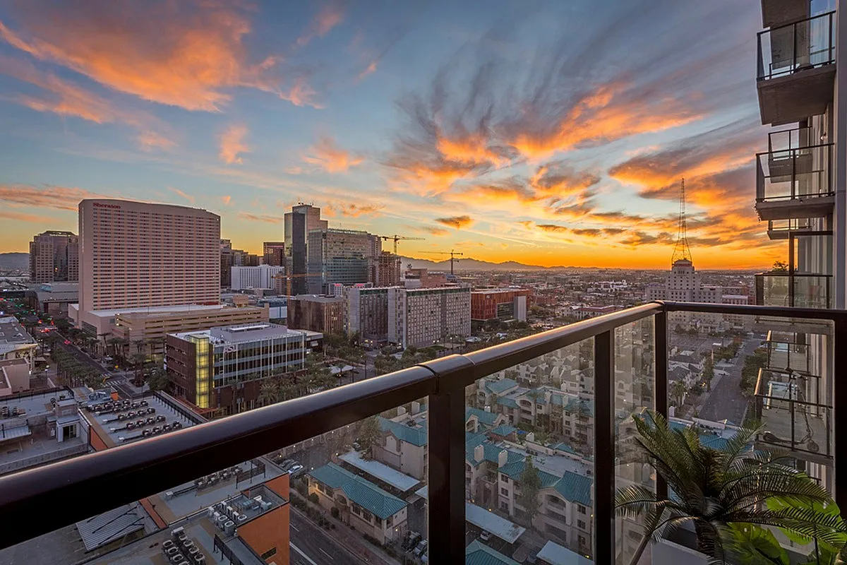 Breathtaking urban skyline view from a modern apartment balcony at sunset, featuring vibrant skies and a bustling cityscape.