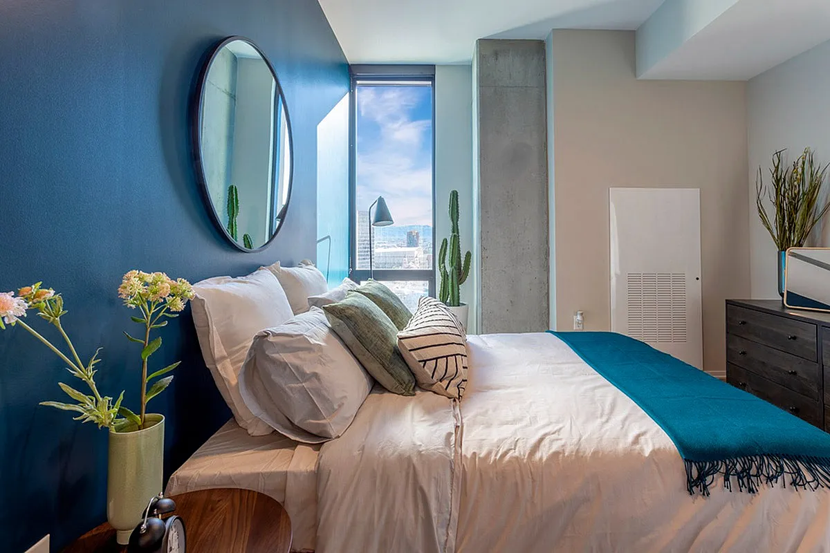 Chic bedroom with a stylish blue accent wall, modern decor, and a bright window view enhancing the airy, tranquil space.