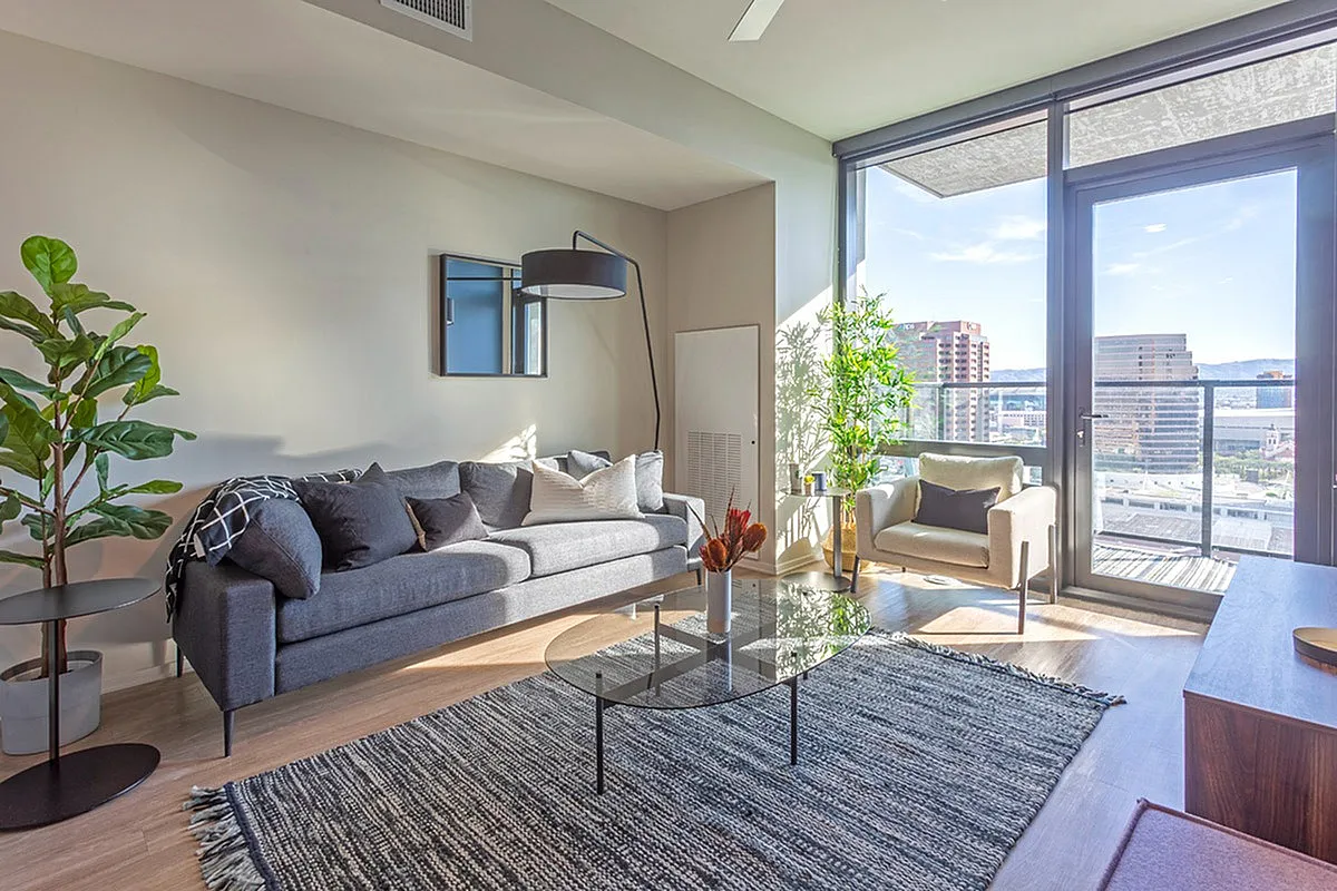 Bright and modern living room with a stylish gray sofa, contemporary armchair, and floor-to-ceiling windows providing stunning city views.