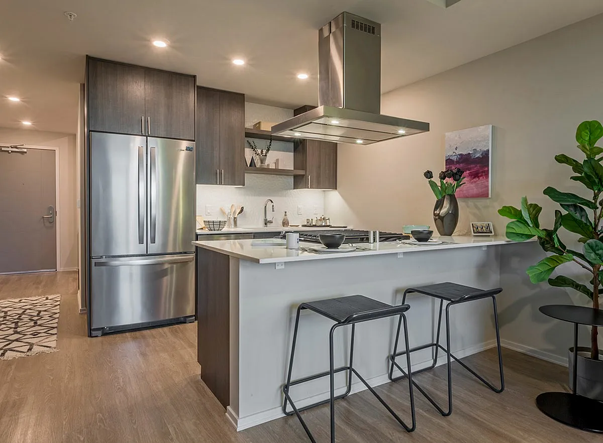 Modern kitchen with sleek stainless steel appliances, elegant cabinetry, and a chic breakfast bar with stylish stools, complemented by warm hardwood flooring and contemporary decor.