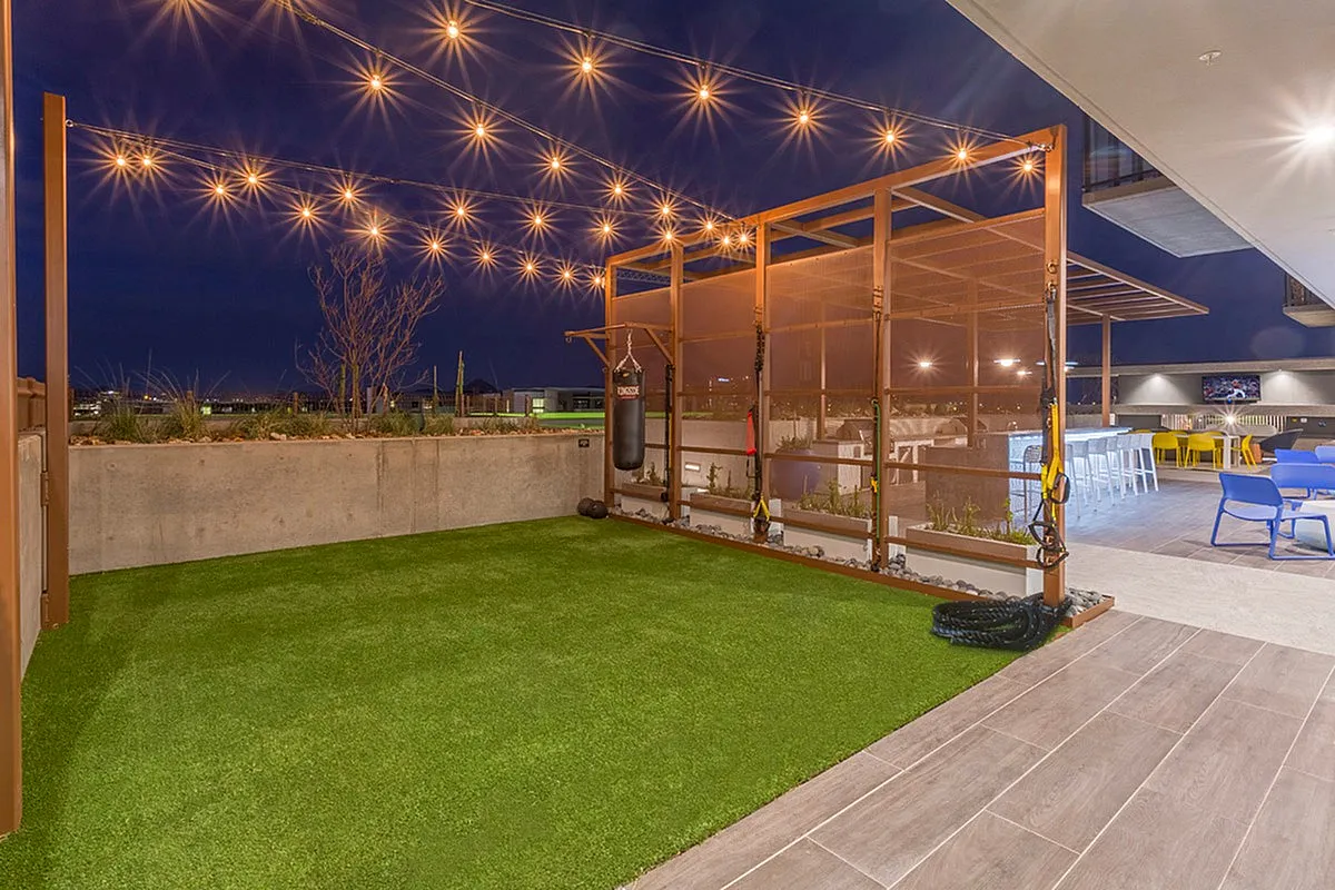 Luxurious rooftop patio showcasing a stylish outdoor gym area with string lights, vibrant seating, and captivating night views.