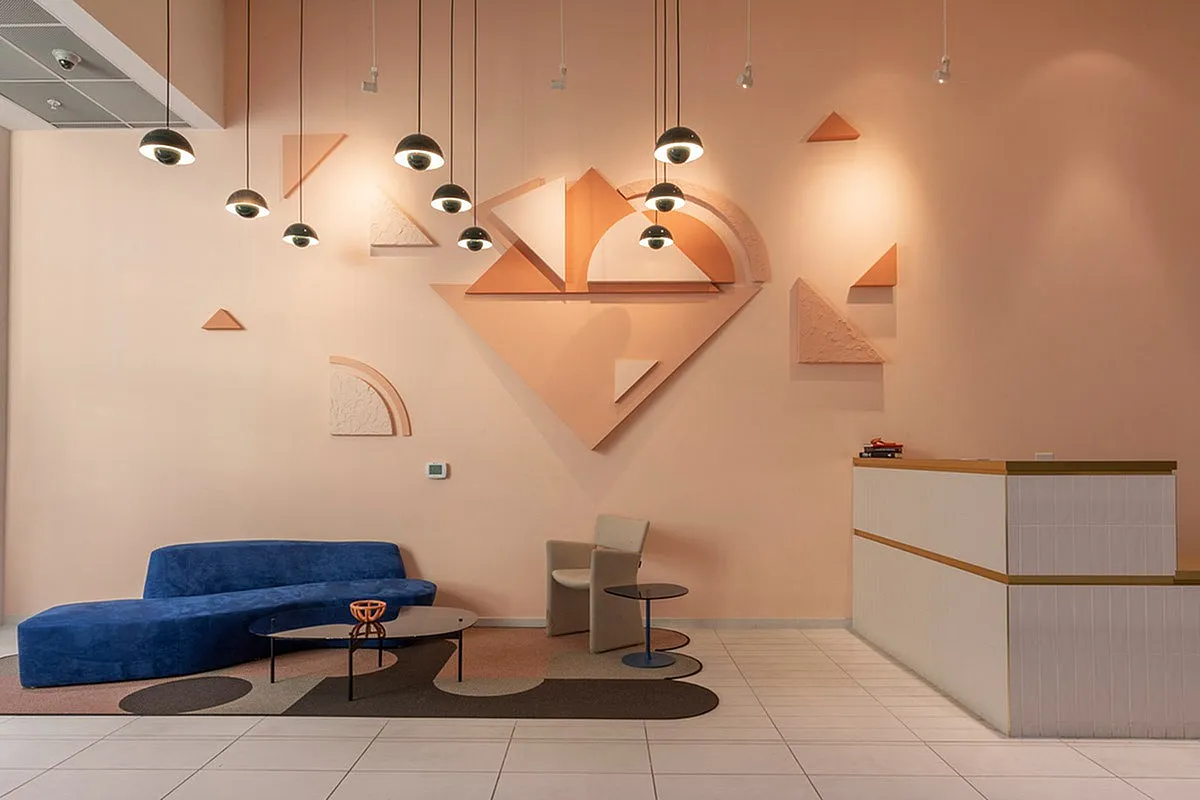 Modern lobby space featuring a chic blue sofa, artistic geometric wall decor, and elegant pendant lighting.