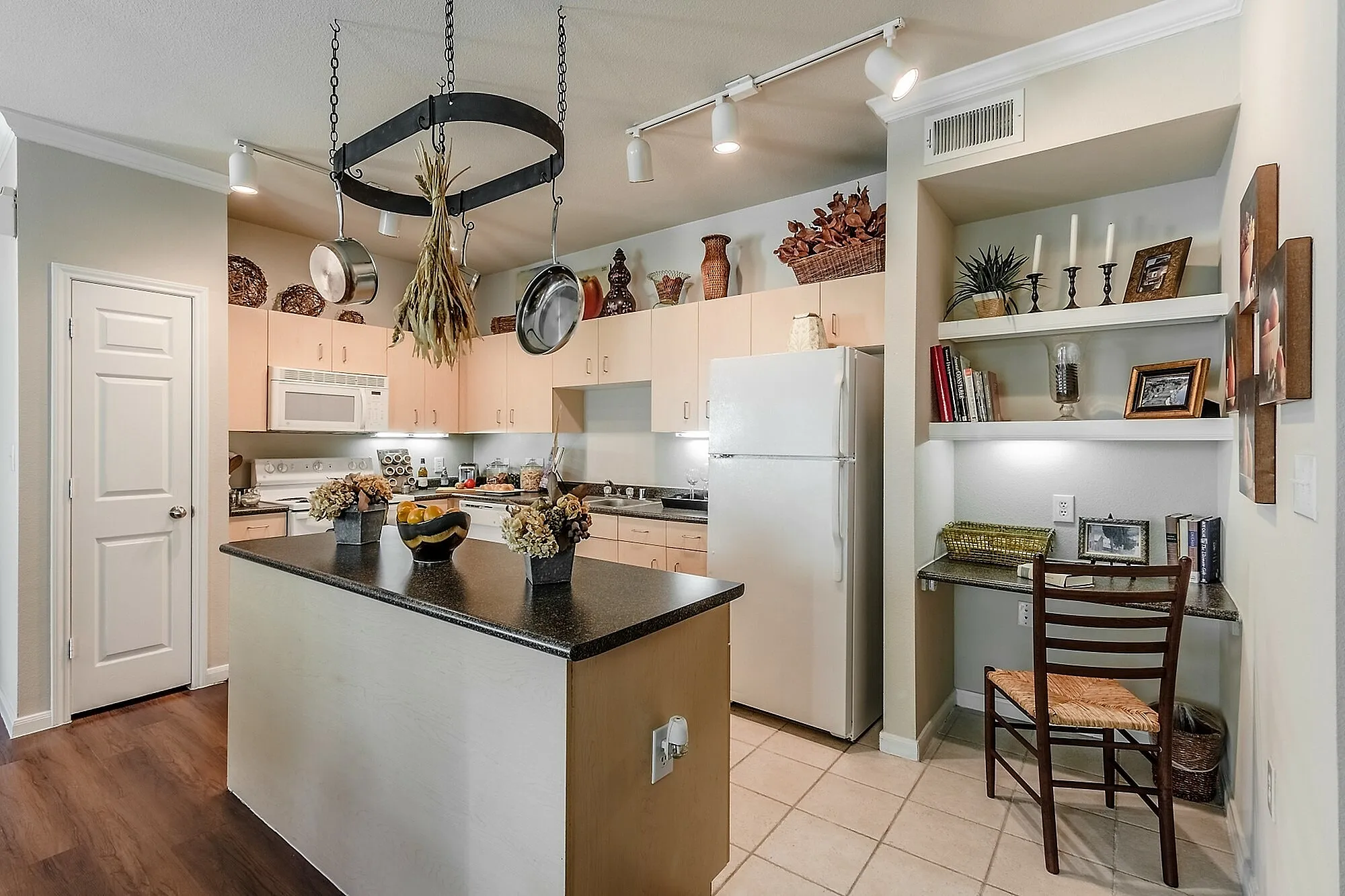 Charming kitchen space with modern lighting, a decorative island, and built-in shelves offering a cozy ambiance.
