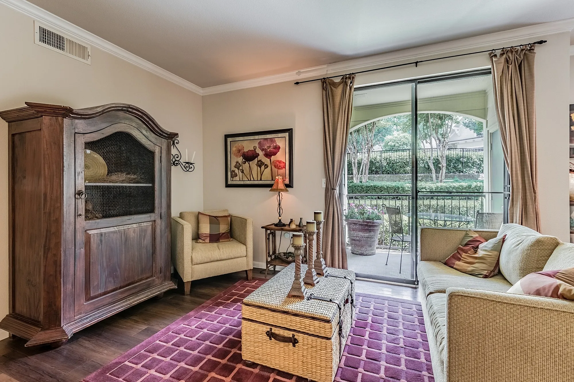 Cozy living room with elegant decor, featuring a plush couch, classic wooden cabinet, and a large window overlooking a serene garden patio.