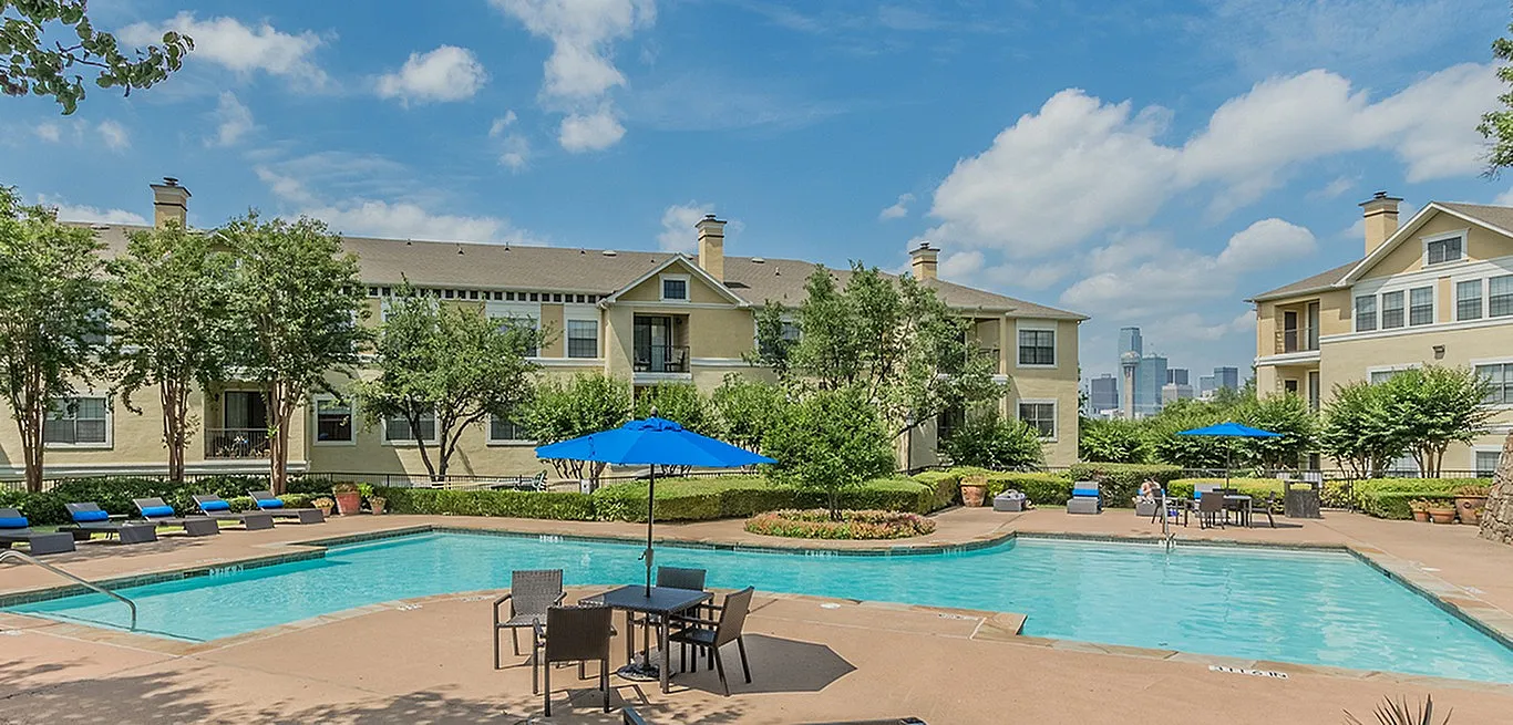 Beautiful apartment complex with a sparkling pool, surrounded by lush greenery and city skyline views.