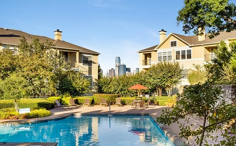 Charming apartment complex with a sparkling pool, lush gardens, and a stunning cityscape view.