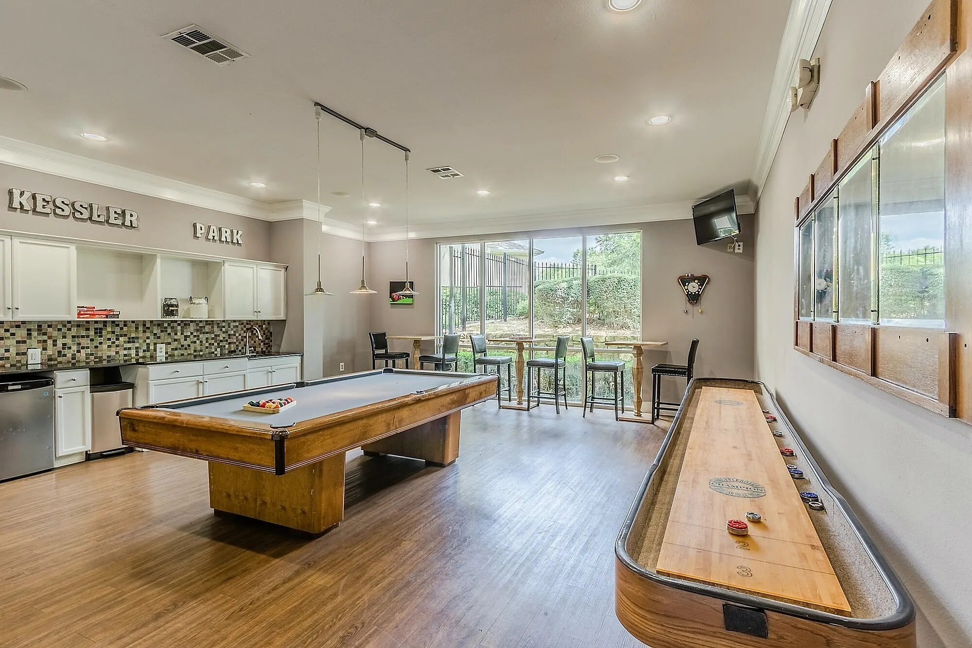 Spacious game room with pool and shuffleboard tables, stylish bar seating, and modern kitchen area.