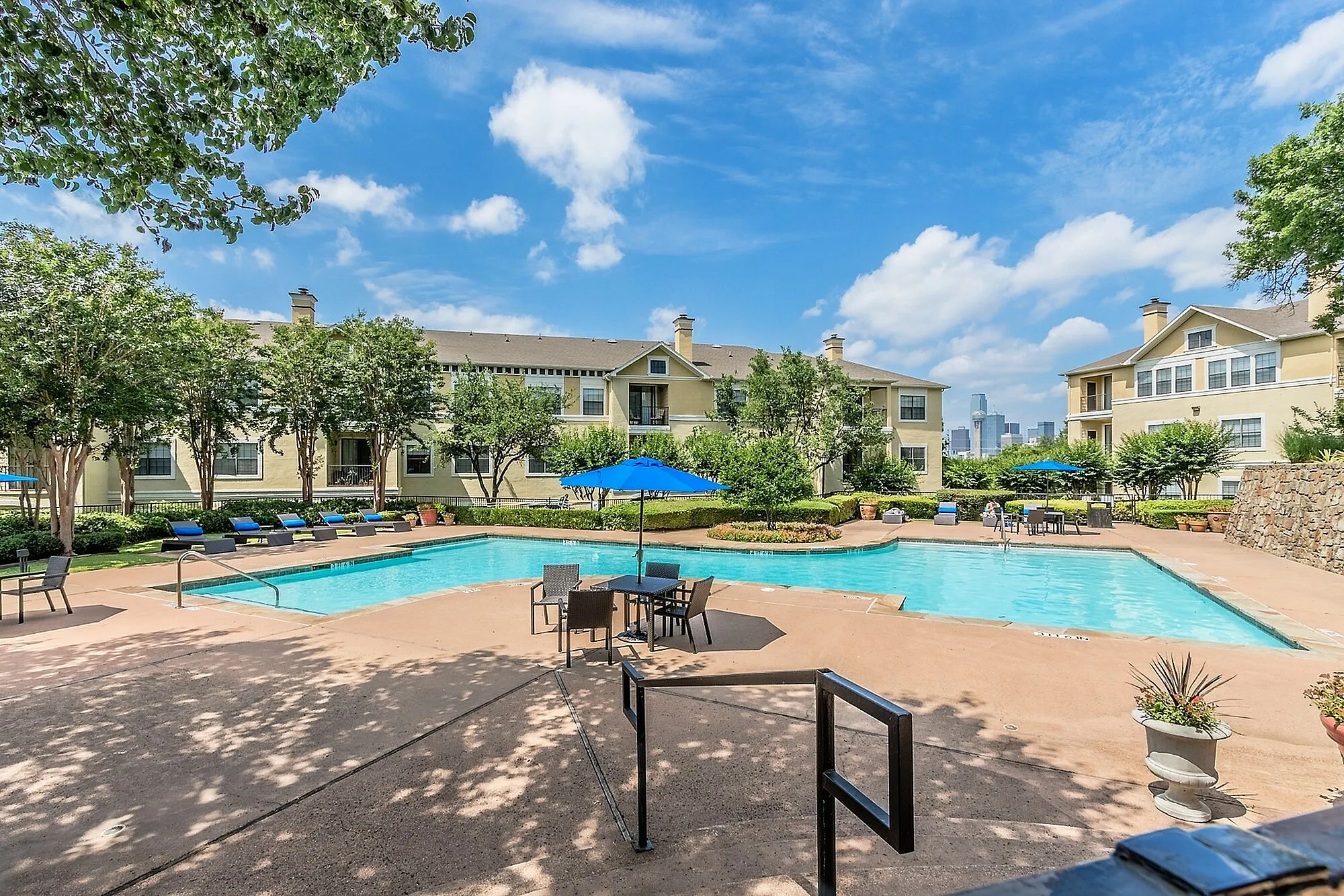Inviting residential community with serene swimming pool, lush greenery, and spacious lounging areas under a bright blue sky.