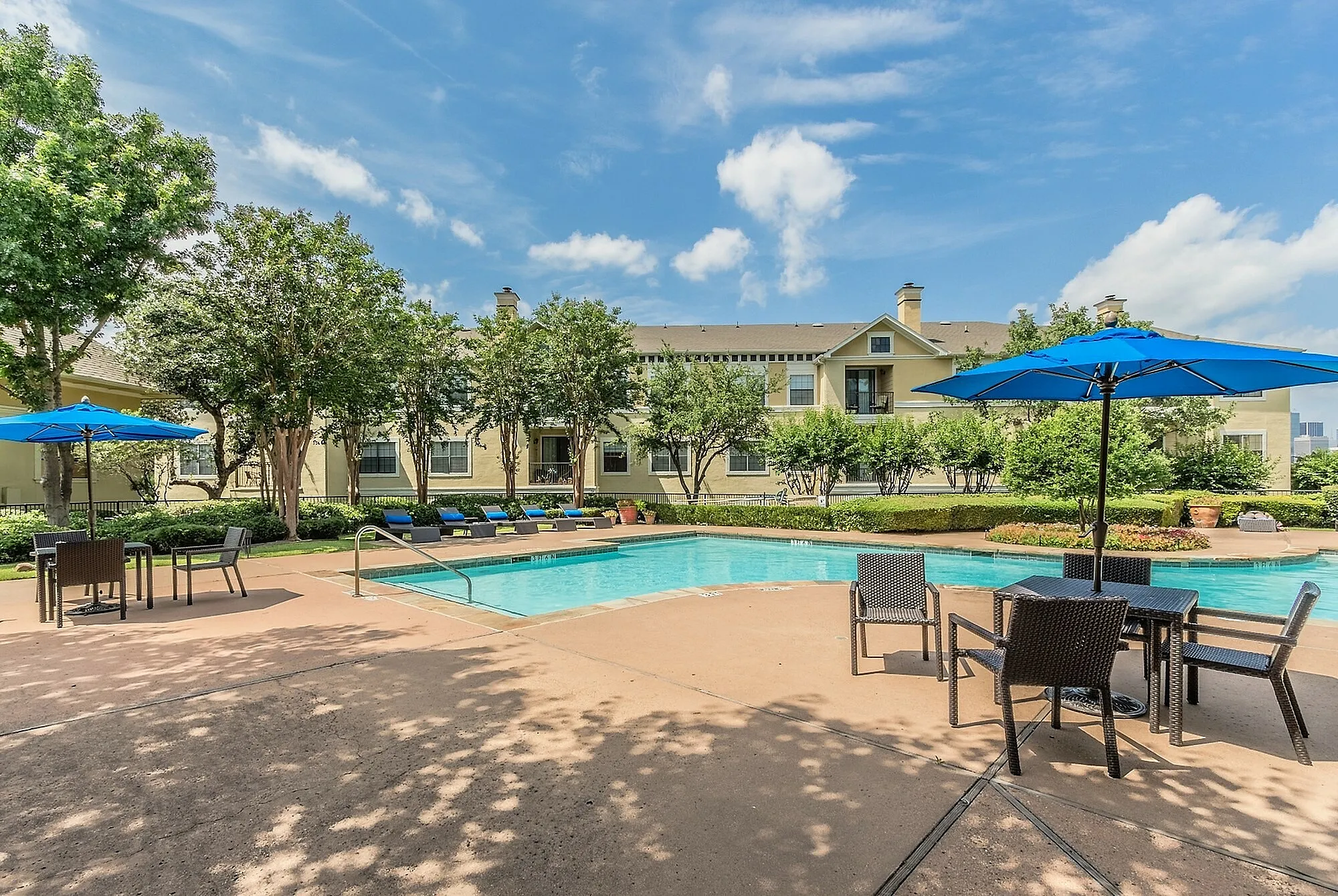 Charming apartment view showcasing a sparkling outdoor pool with stylish patio seating under vibrant blue umbrellas.