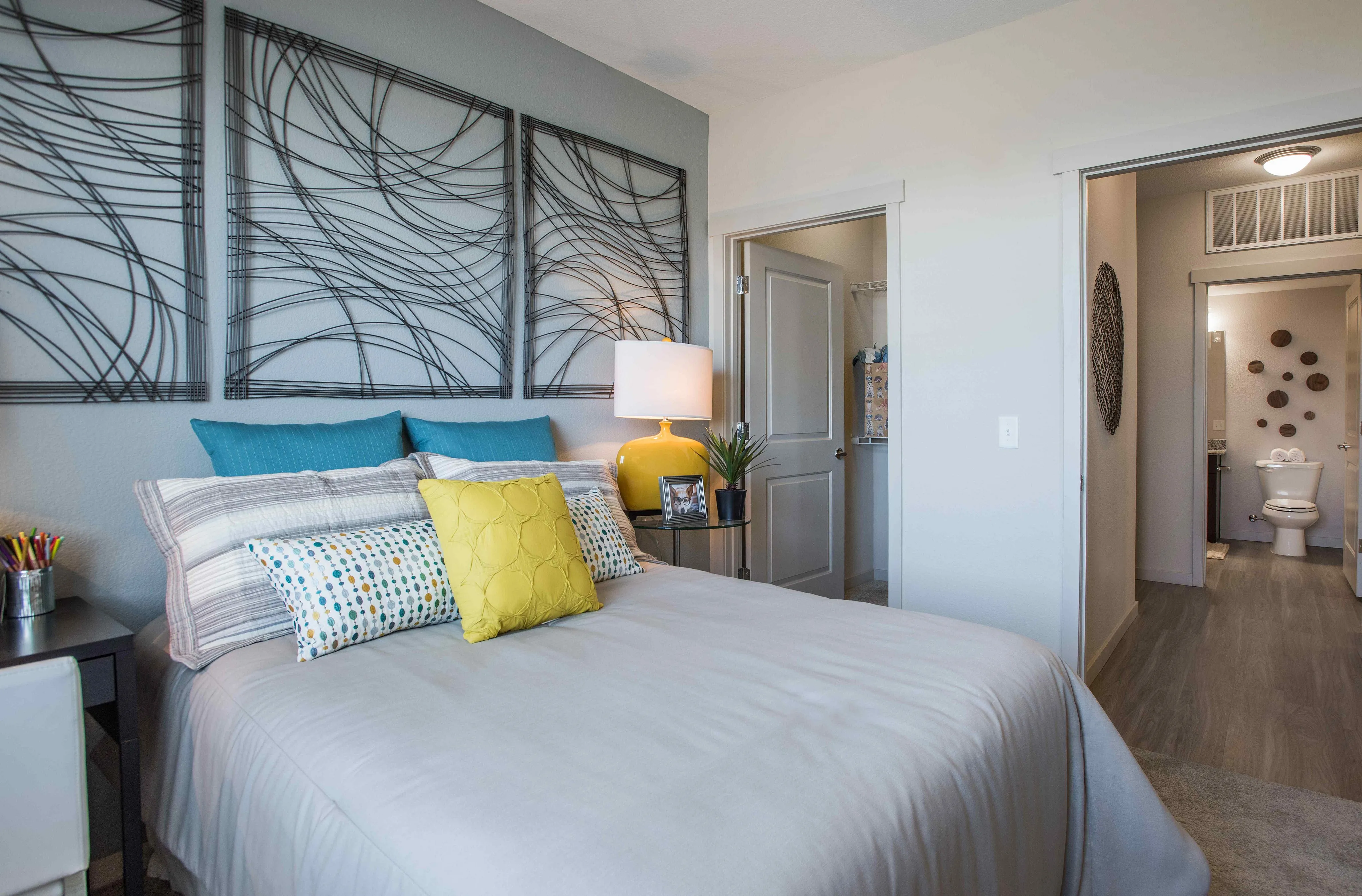 Inviting bedroom with elegant decor, modern art, and bright accents, featuring a cozy bed with colorful cushions and a stylish nightstand.
