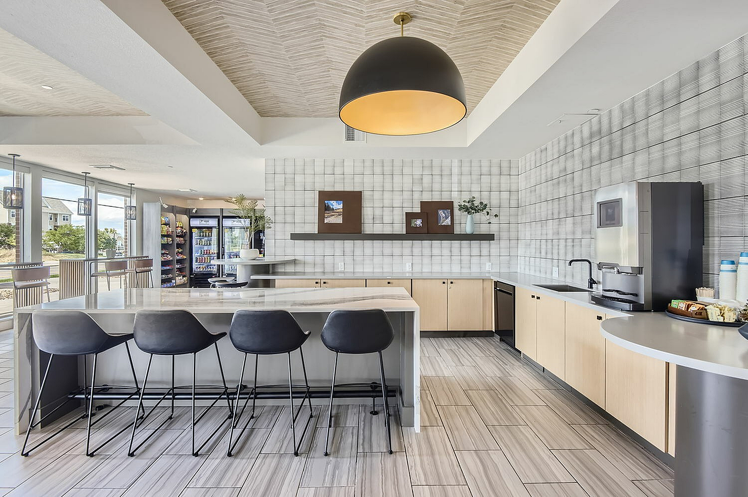 Modern kitchen and lounge area with sleek countertops, stylish bar seating, and large windows offering a bright, inviting atmosphere.