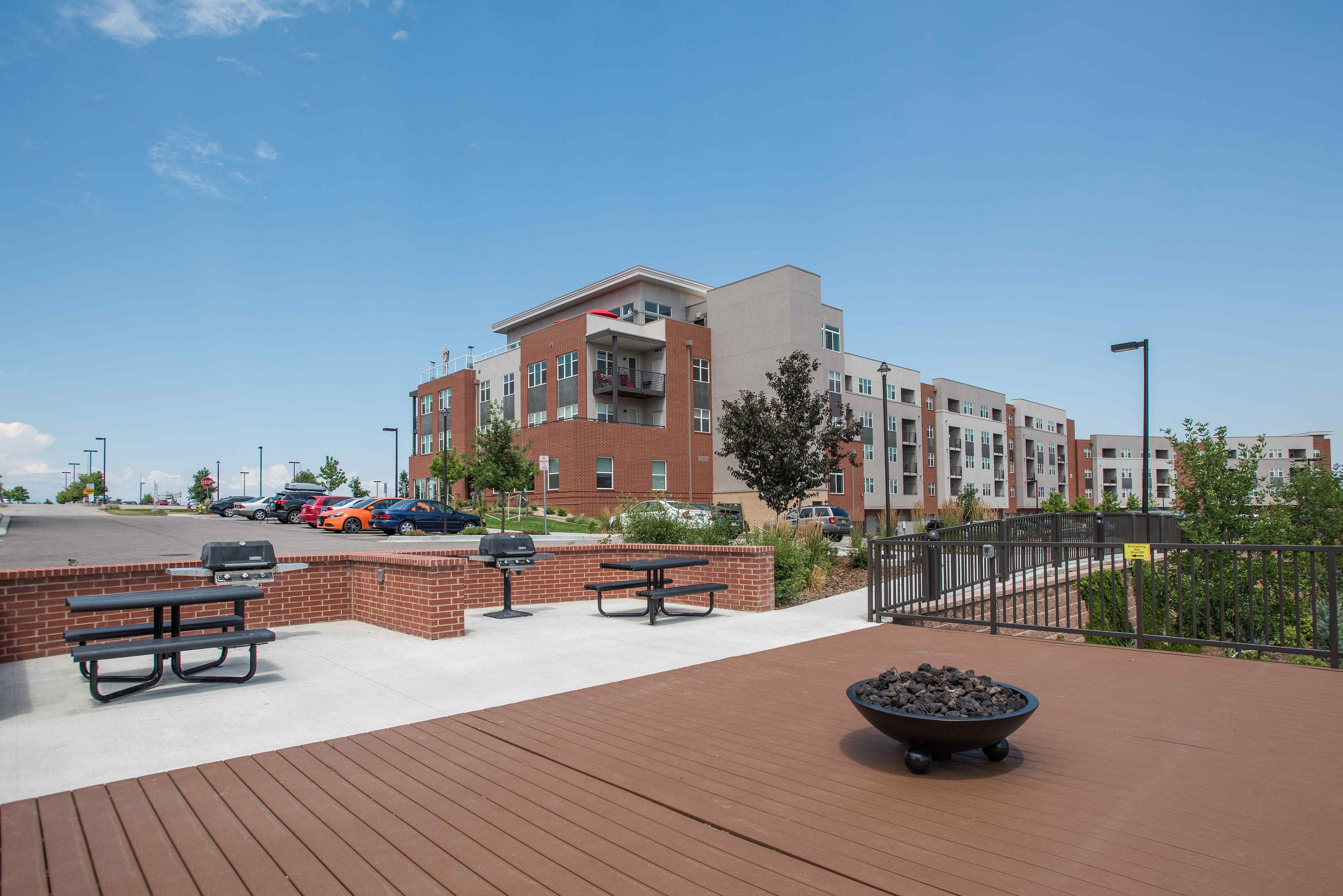 Modern apartment complex with brick facade, outdoor seating, and vibrant landscaping under clear blue skies.
