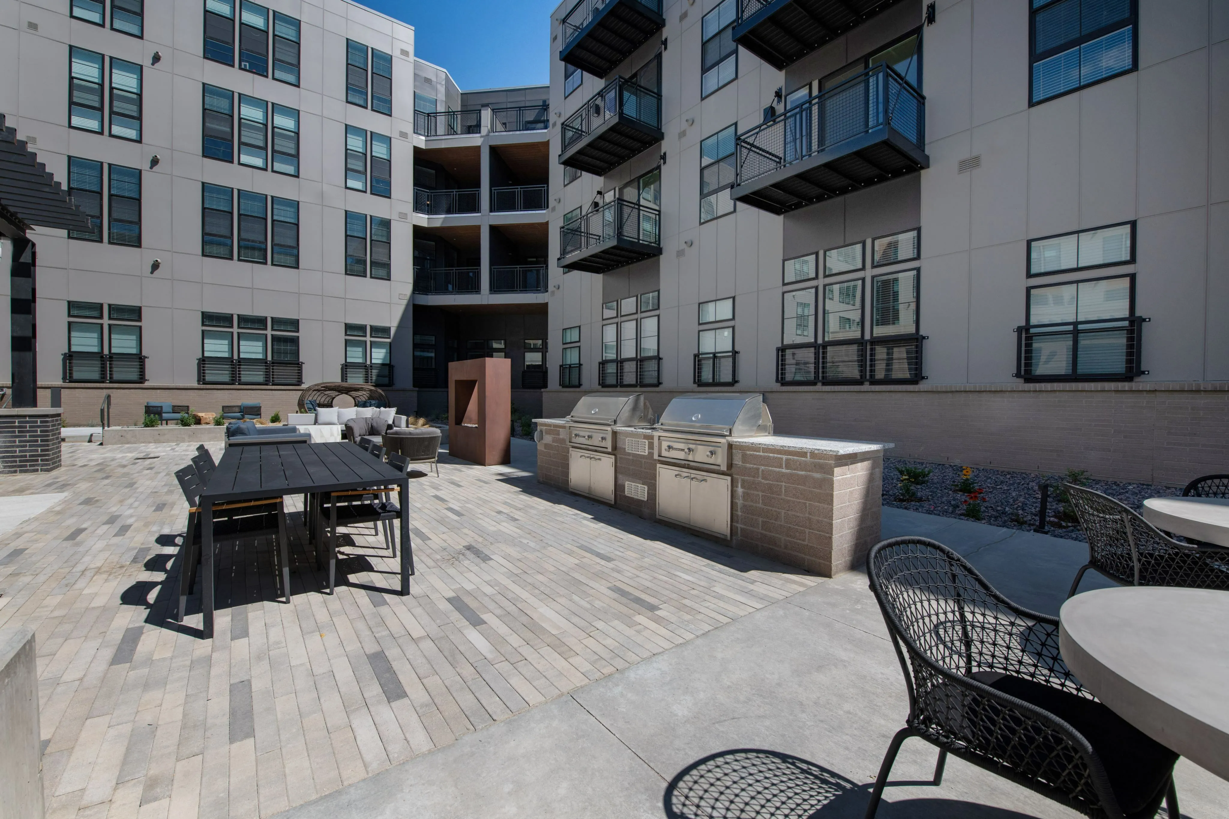 Modern apartment courtyard featuring stylish outdoor seating, sleek dining area, and state-of-the-art grills for a luxurious lifestyle.