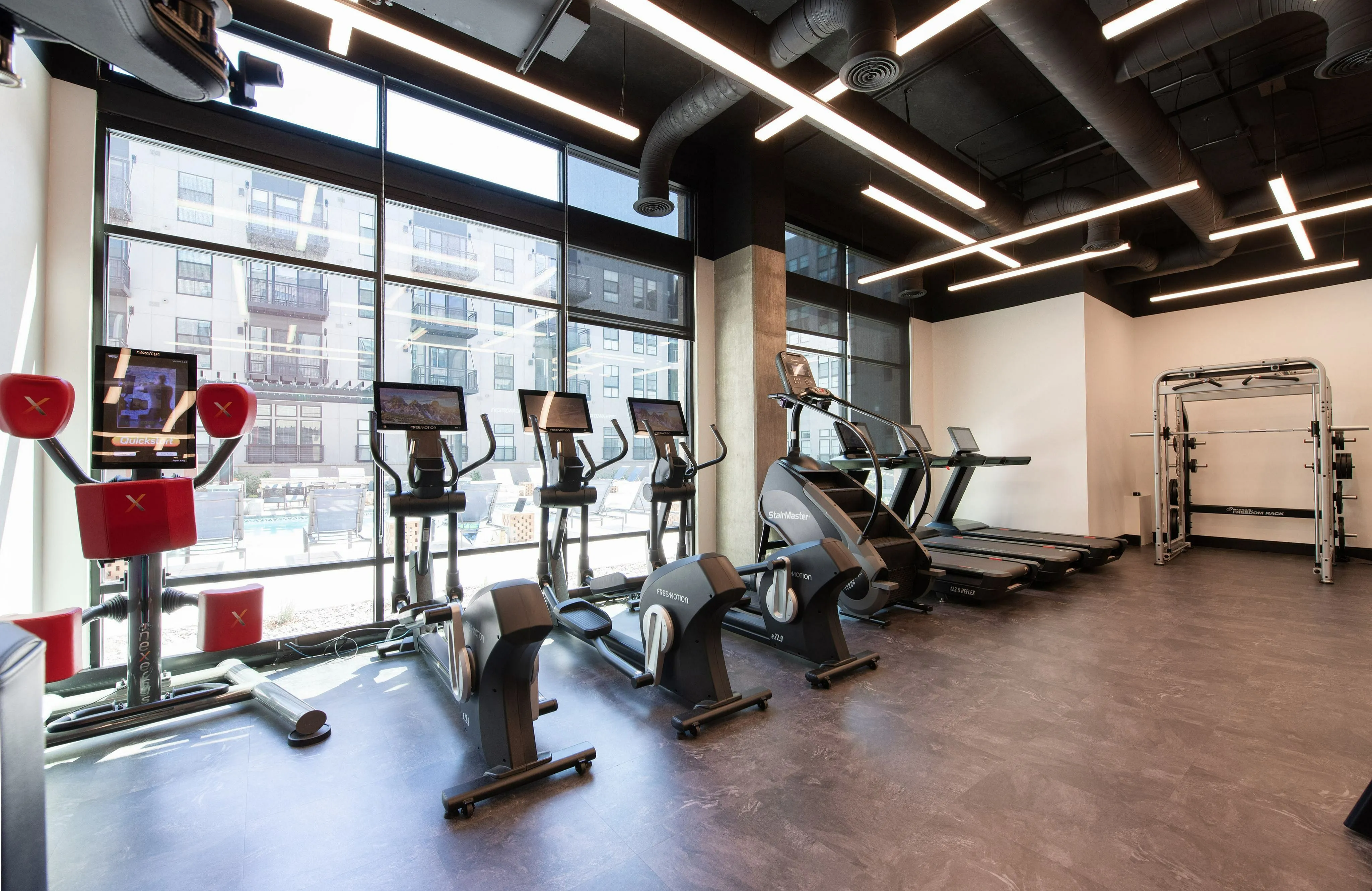 Modern, sunlit fitness center equipped with state-of-the-art exercise machines and large windows offering a dynamic city view.