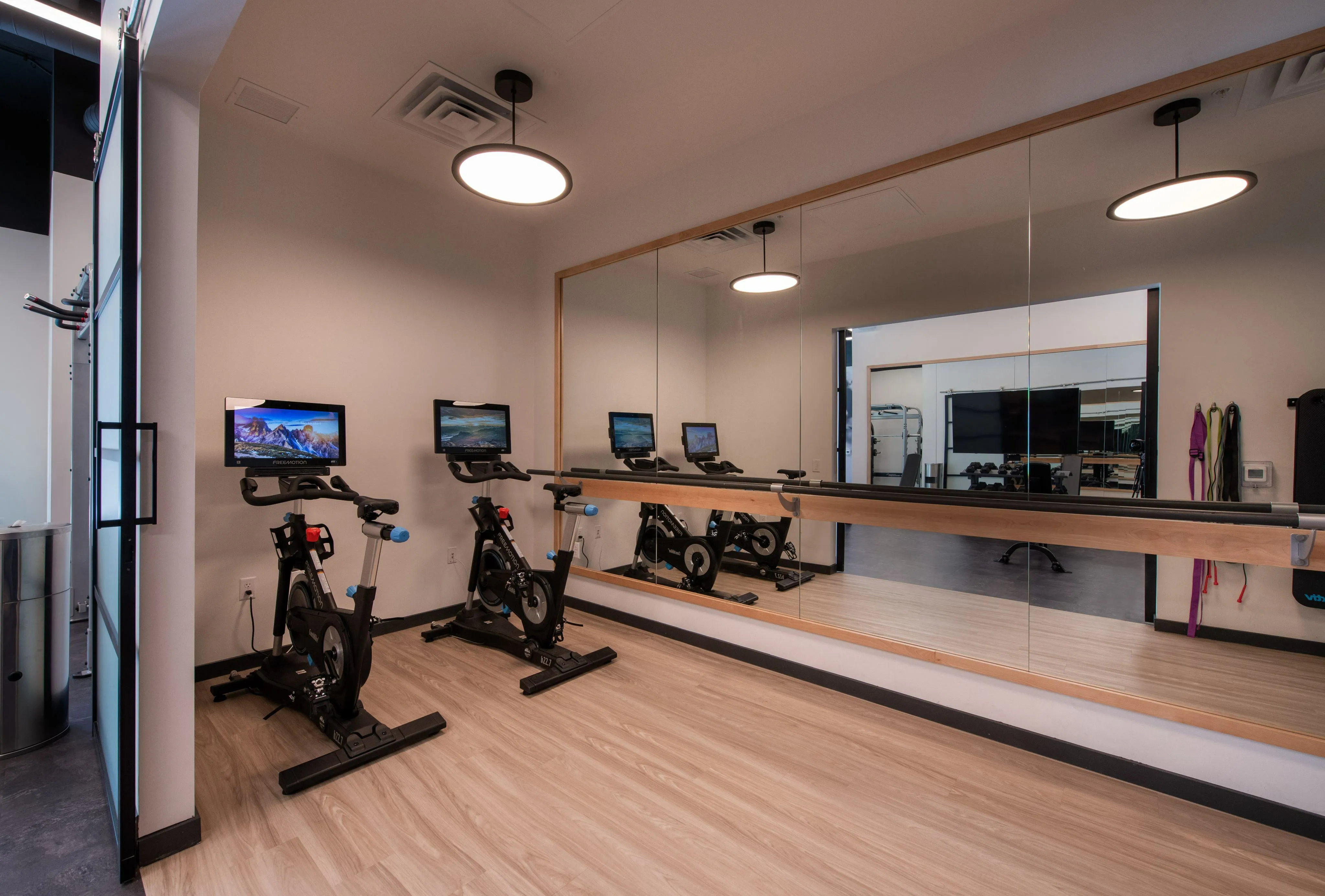 Modern fitness room with two high-tech stationary bikes, wall-length mirror, and sleek wooden flooring for an inspiring workout atmosphere.