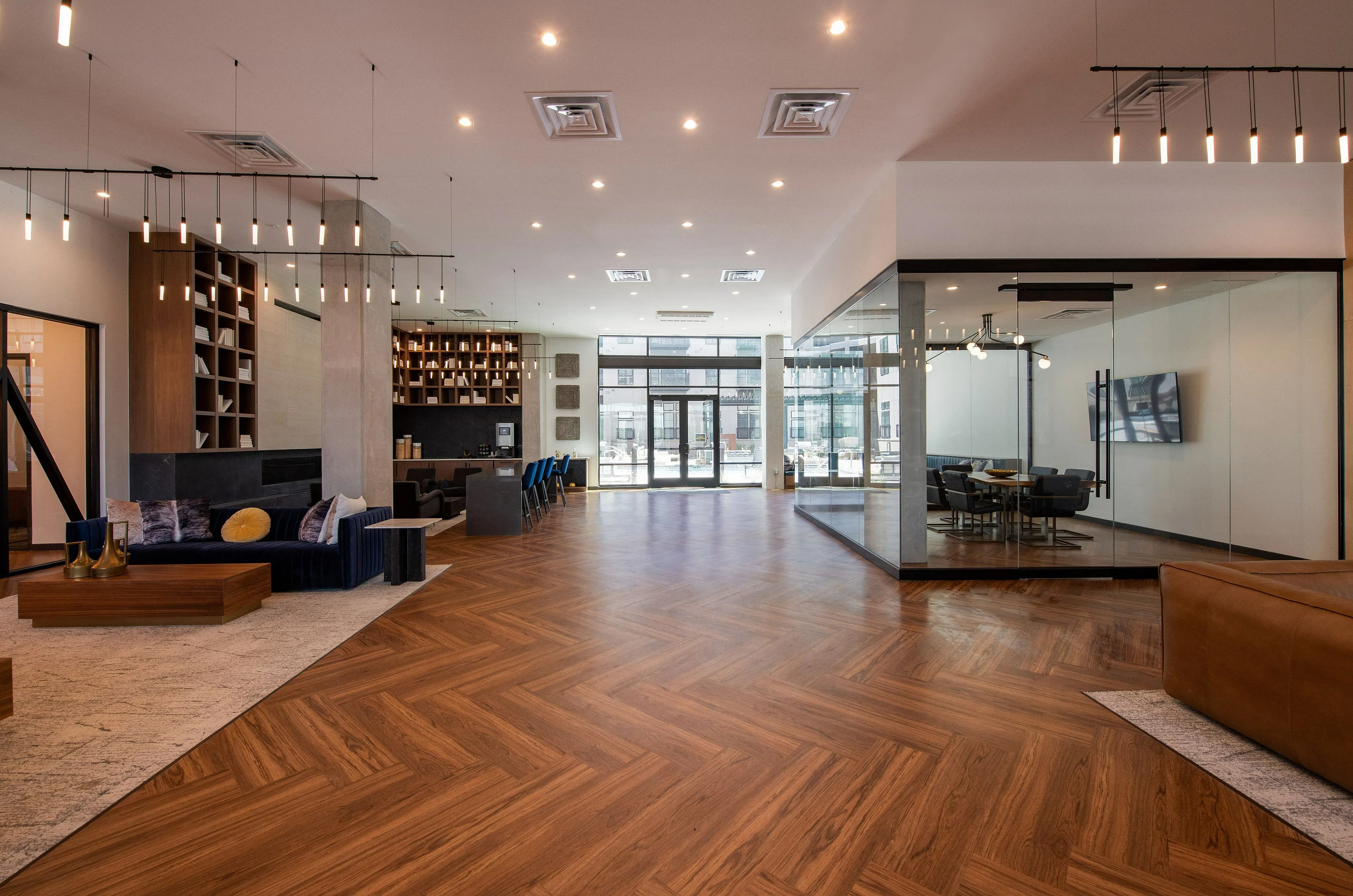 Luxurious open-concept living space featuring elegant herringbone wood flooring, modern lighting, a contemporary seating area, and a chic glass-walled conference room.