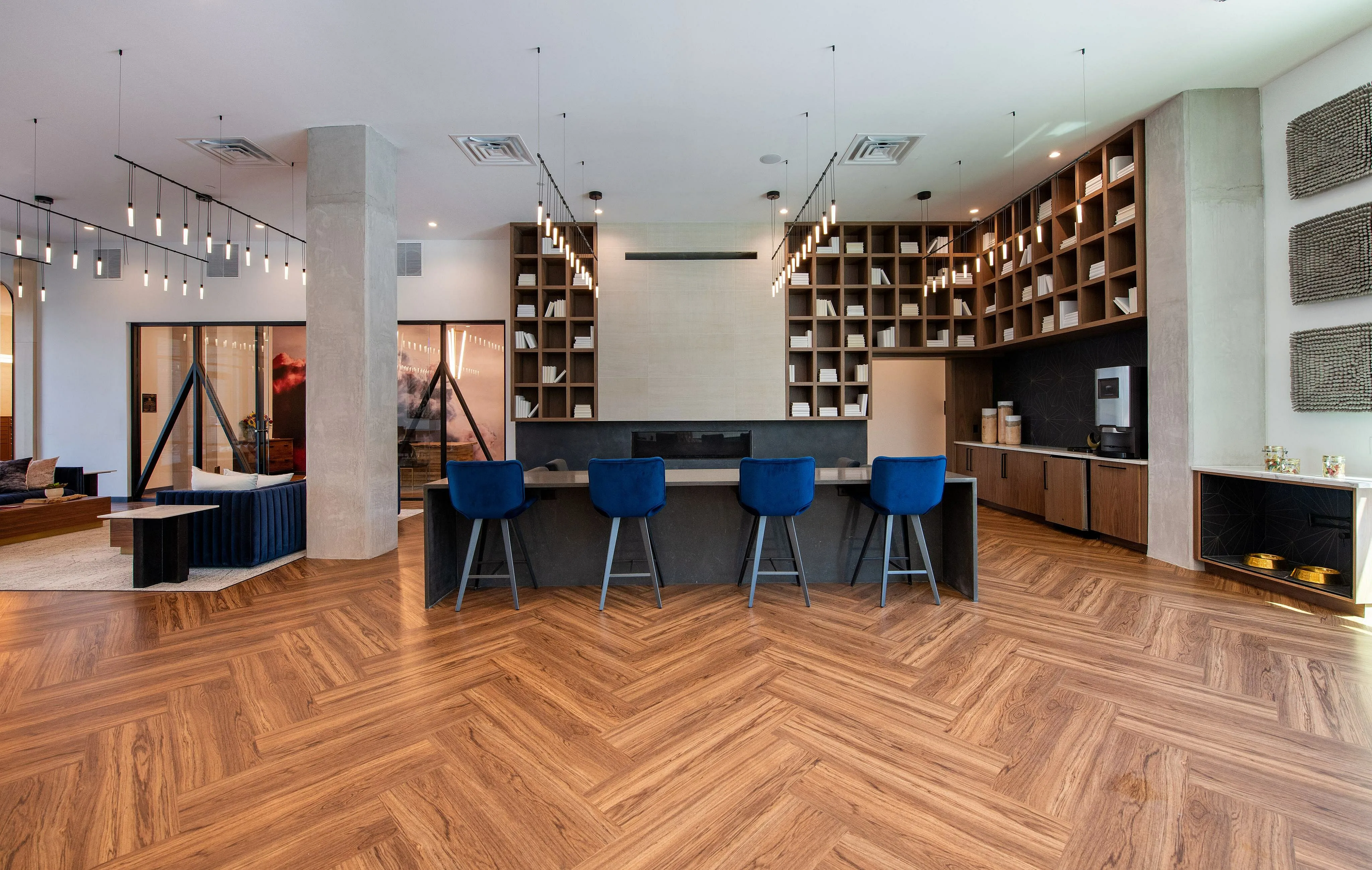 Modern apartment lounge with sleek wooden flooring, stylish bar seating, and geometric shelving, offering a chic and inviting atmosphere.