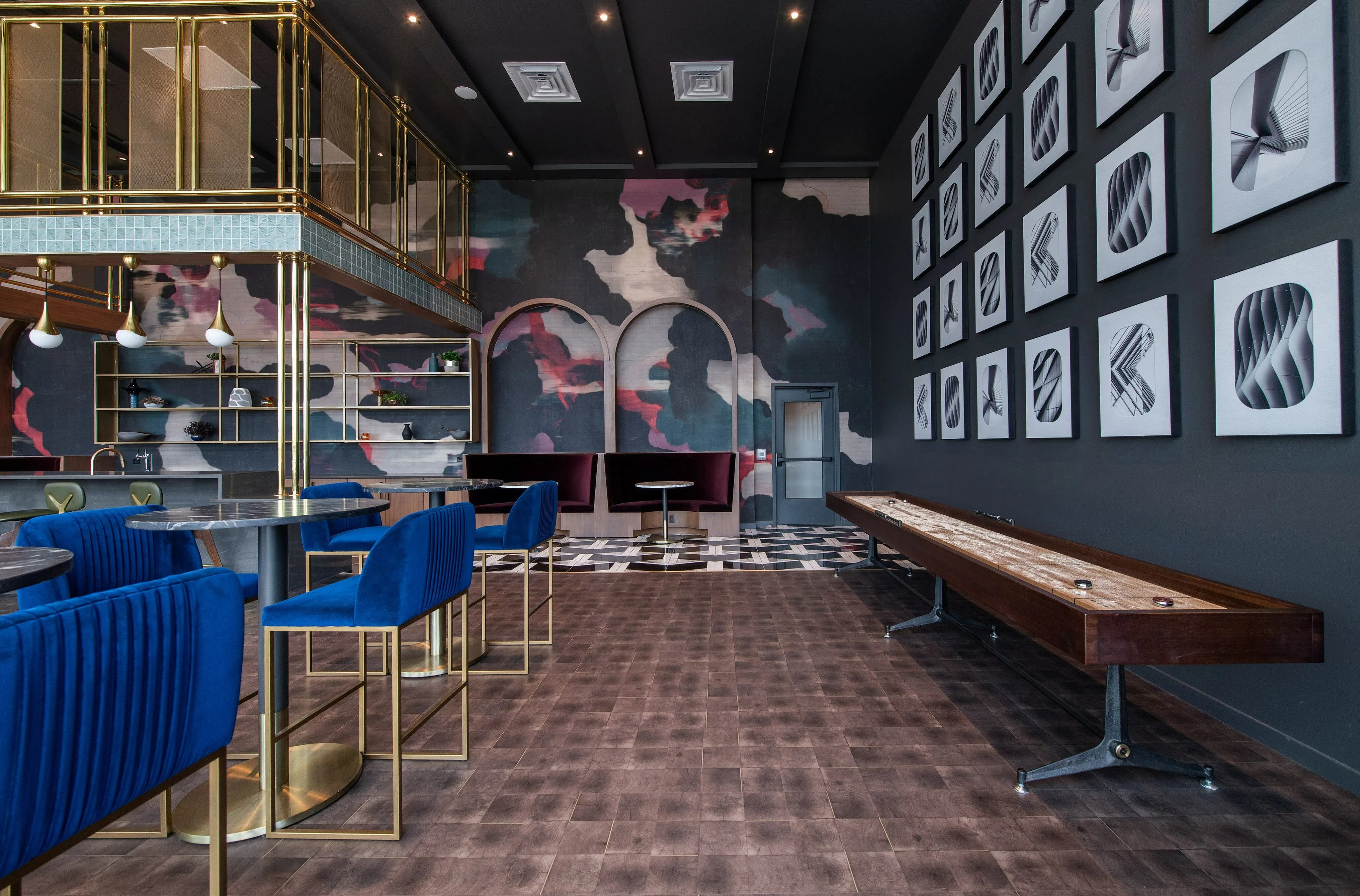 Modern and artistic lounge with sophisticated decor, featuring elegant blue velvet seating, chic pendant lights, and a sleek shuffleboard table.