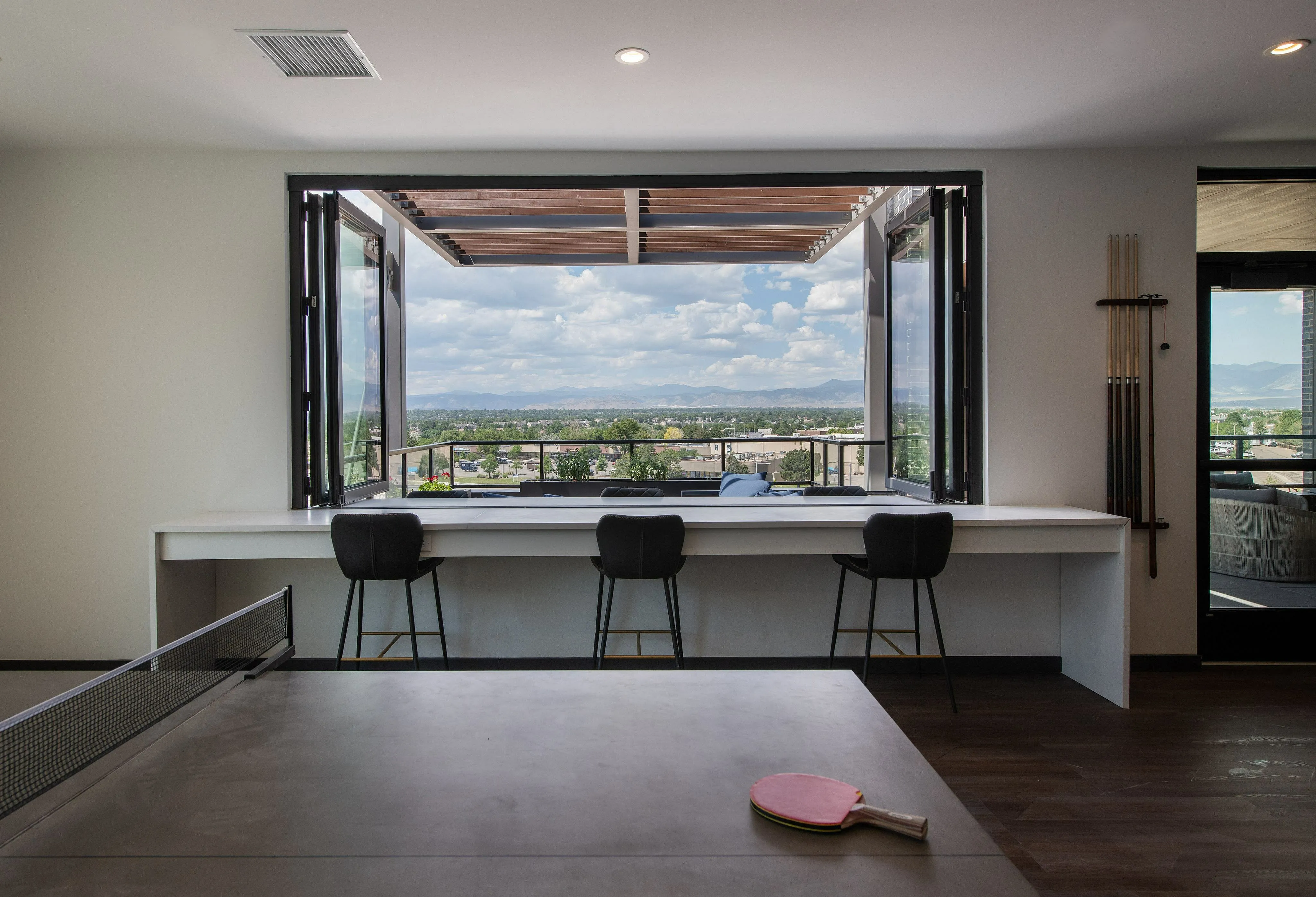Modern apartment with indoor ping-pong table, expansive open window views of scenic landscapes, and sleek bar seating.
