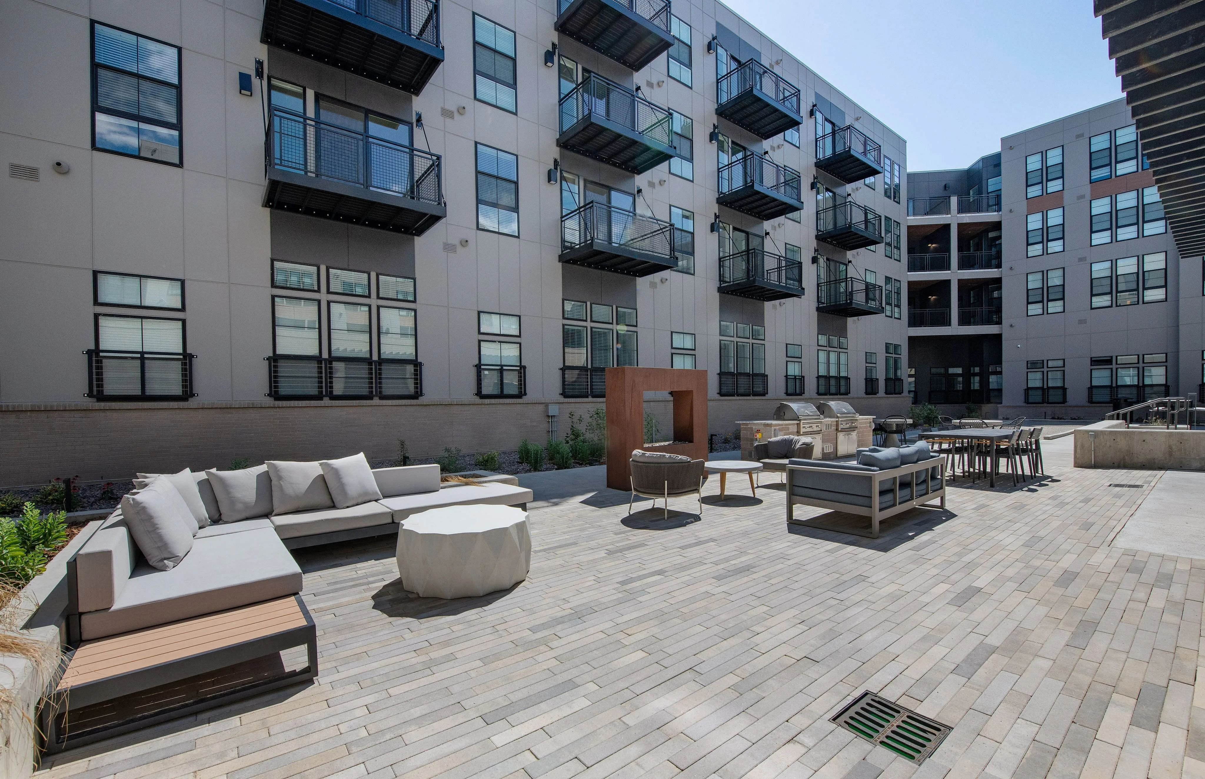 Modern apartment building with stylish balconies, featuring a chic outdoor lounge area with comfortable seating and a grill, perfect for entertaining.