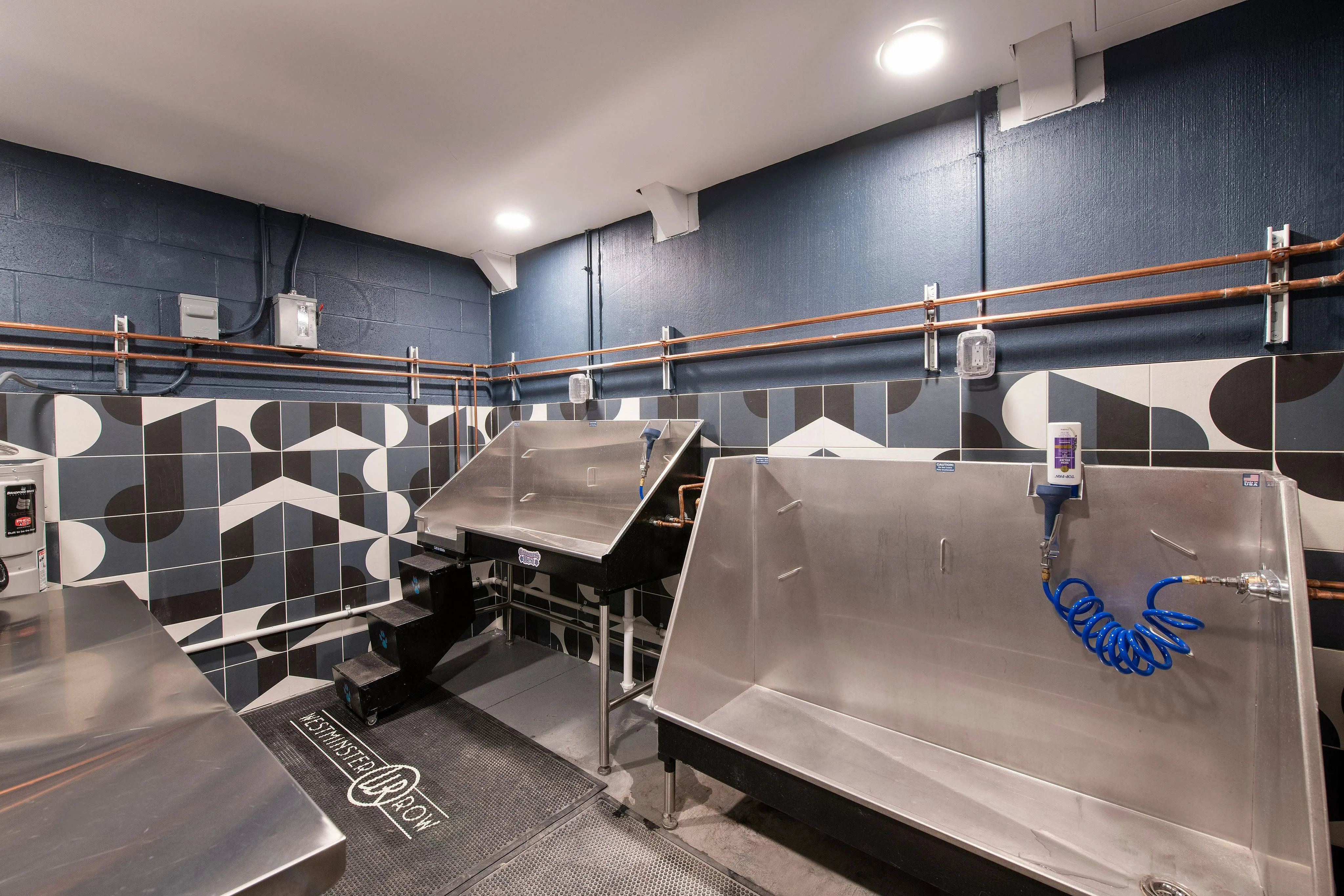 Modern utility room showcasing stylish geometric tiled walls, stainless steel sinks, and sleek lighting for a chic industrial vibe.